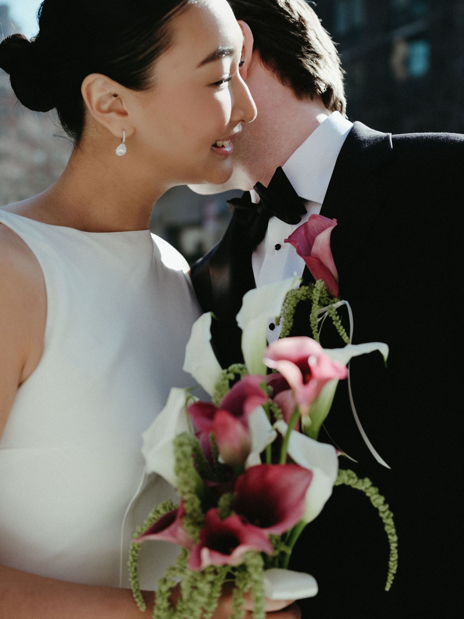 Couple shares intimate moment, bride holds stunning pink and white calla lily bouquet in natural sunlight.