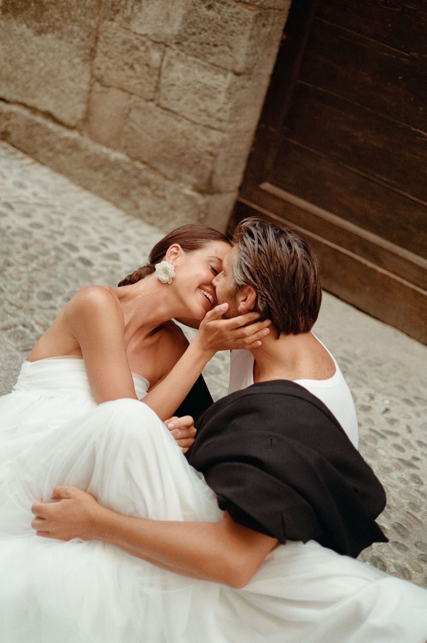 Bride and groom laughing and embracing intimately while lying on cobblestone steps in Italy.