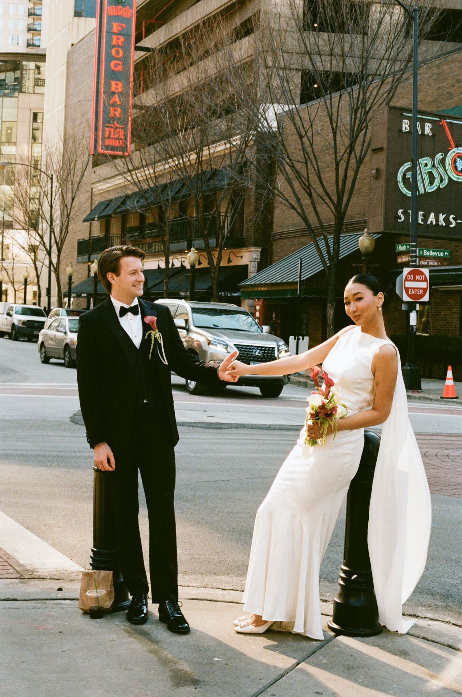 Bride and groom hold hands on a Chicago street corner, with the bride carrying a vibrant bouquet.