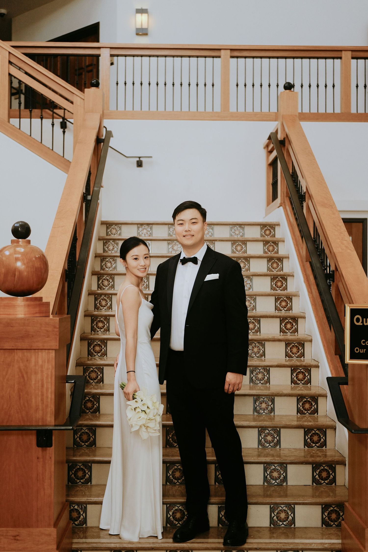 Wedding couple posing on decorative tiled staircase inside elegant venue interior.