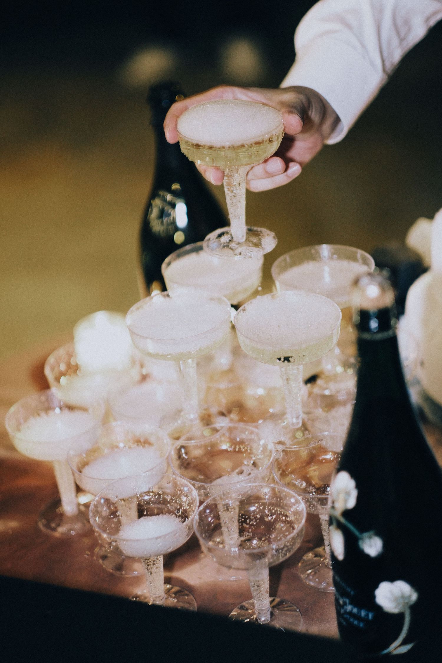 Champagne tower being poured at wedding reception with sparkling coupe glasses and candles.