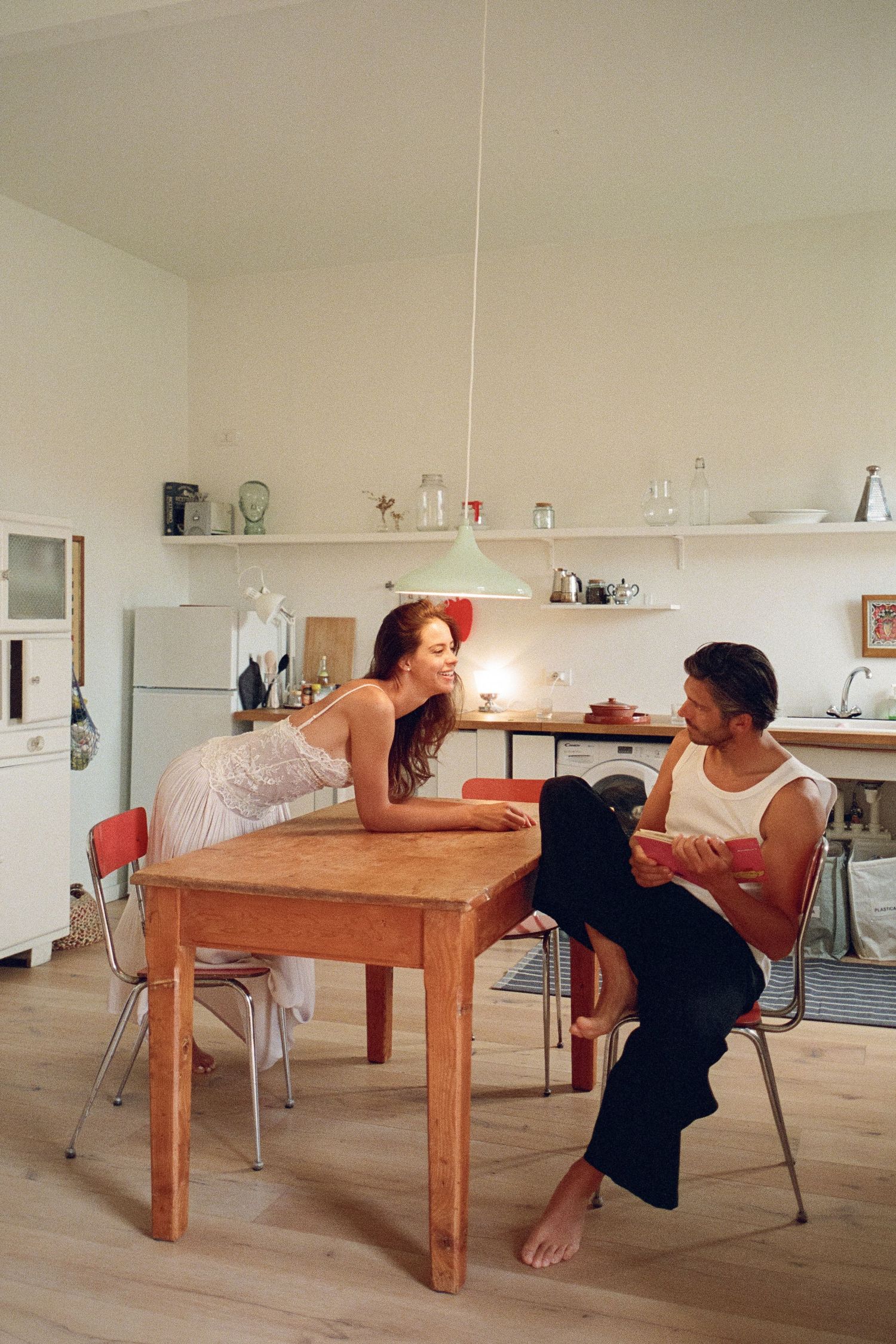 Bride and groom in casual white outfits sharing an intimate conversation at a kitchen table.