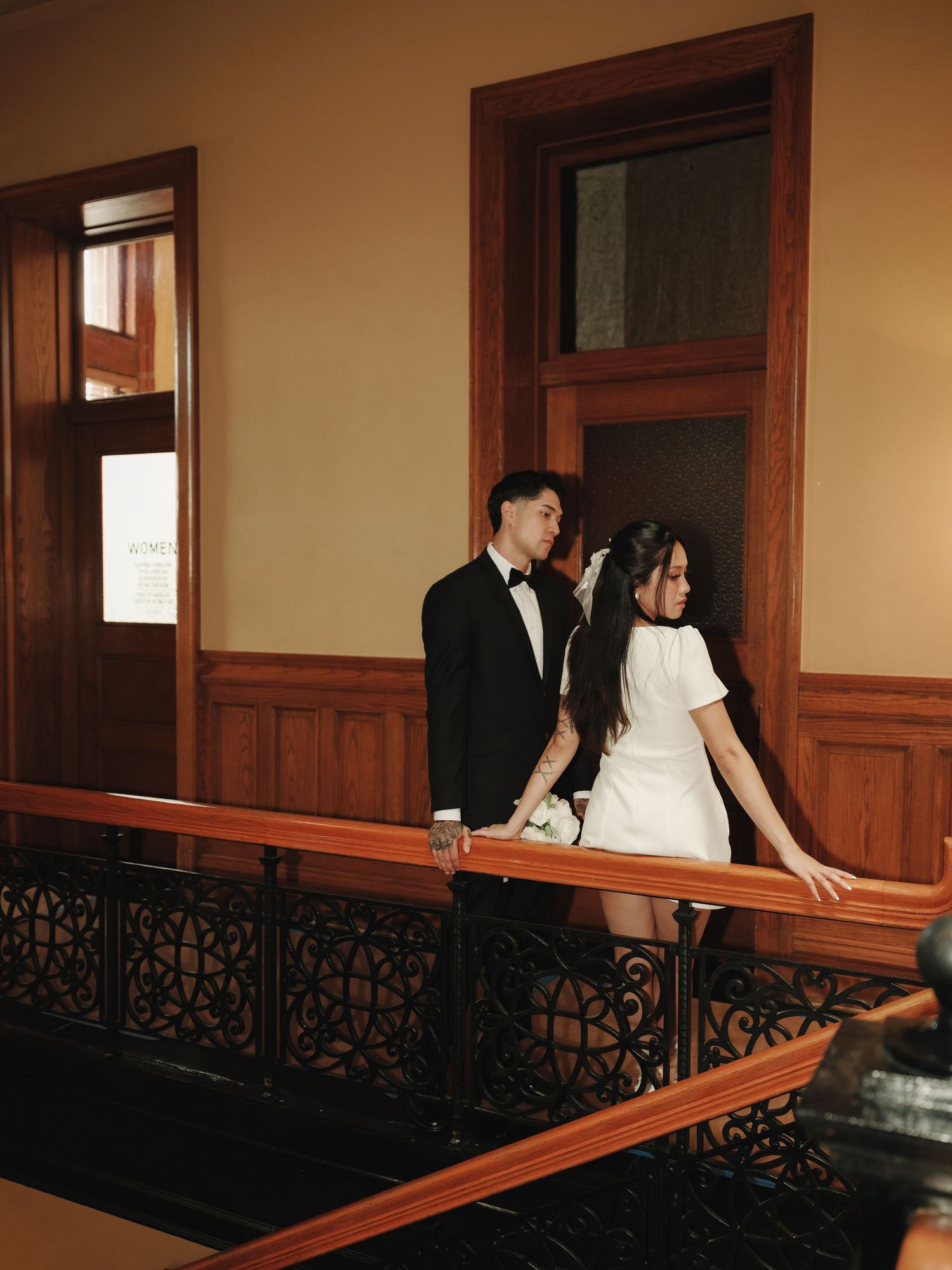 Newlywed couple ascending ornate wooden staircase inside historic courthouse after wedding ceremony.