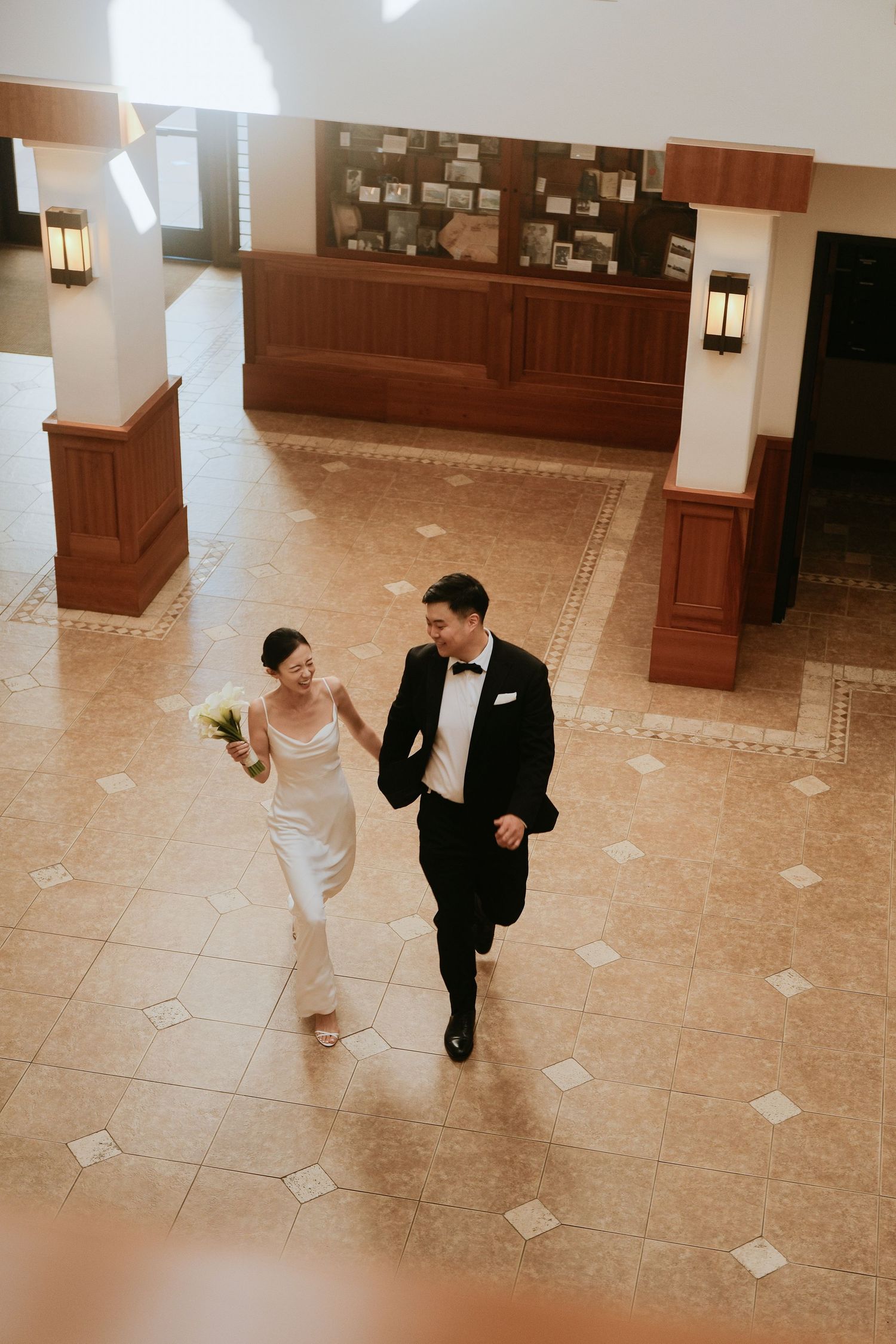 Aerial view of Asian bride and groom walking hand in hand through elegant hotel lobby on their wedding day.