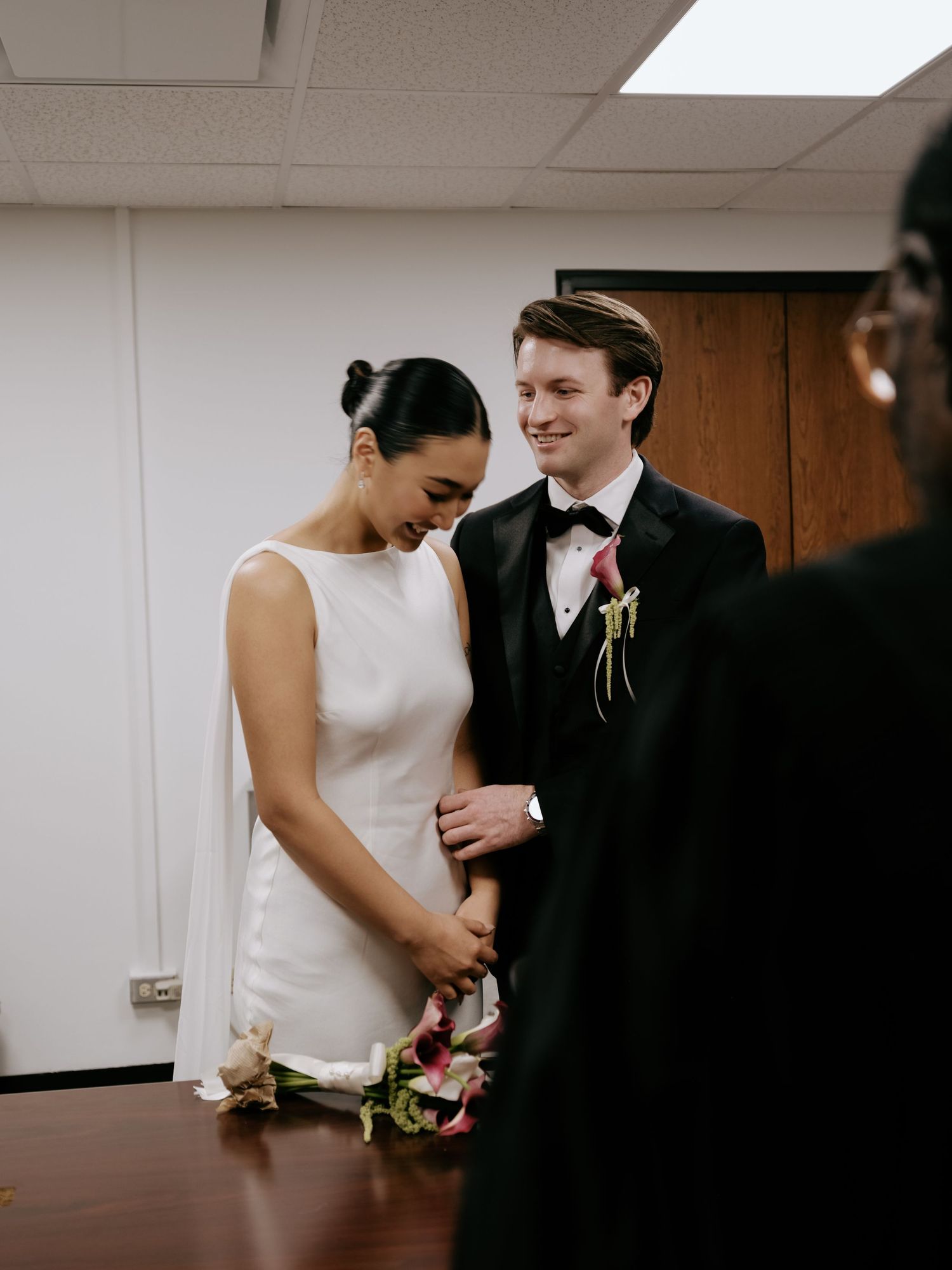 Bride and groom exchange vows at intimate courthouse wedding ceremony, bride in minimalist white gown.