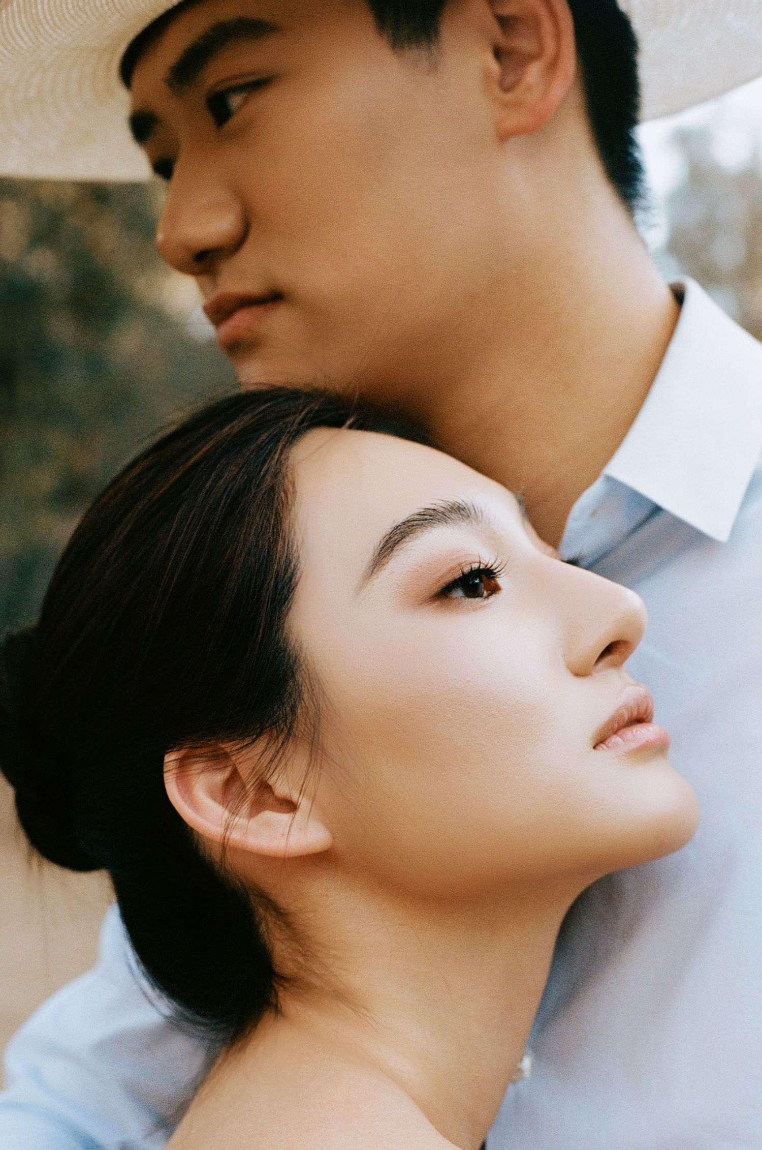 Asian bride leans back against groom wearing a white cowboy hat in a tender close-up portrait.