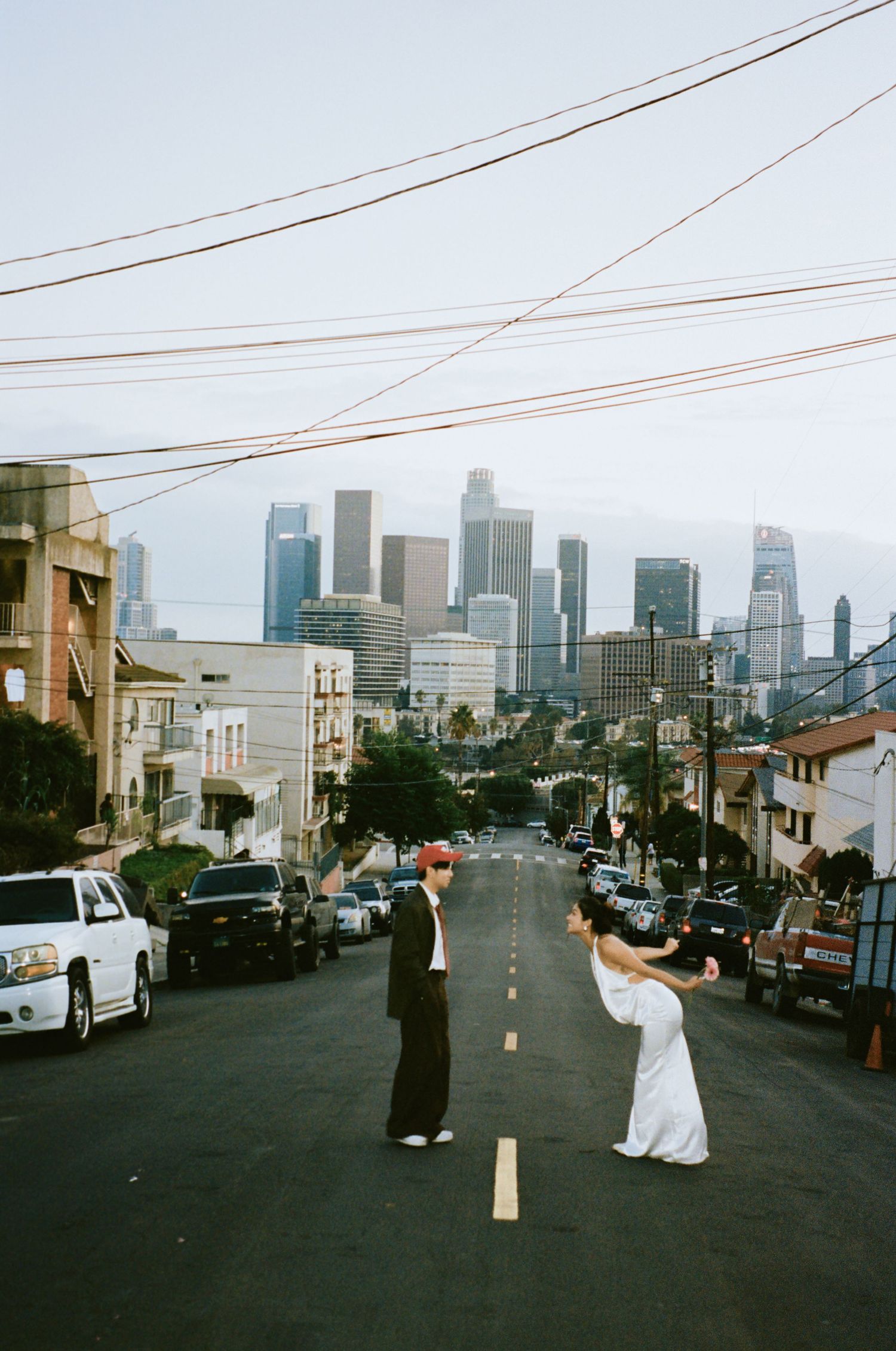 Couple facing each other in middle of city street with dramatic Los Angeles skyline in the background.