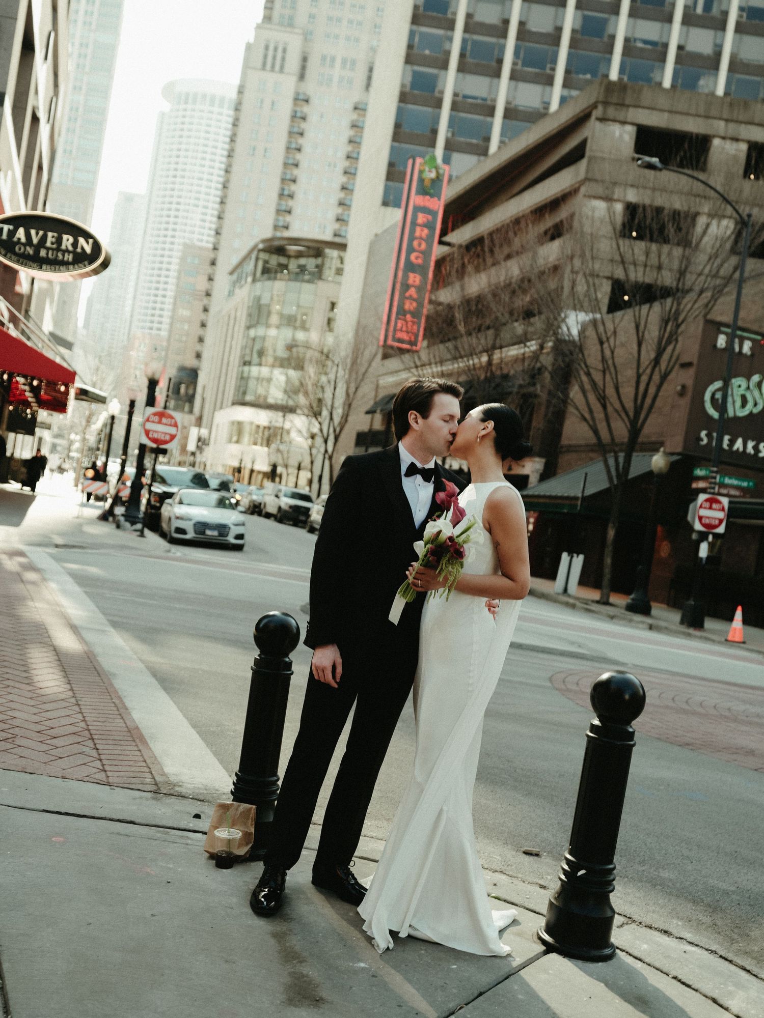 Bride and groom share a kiss on a Chicago street corner with city skyline in the background.