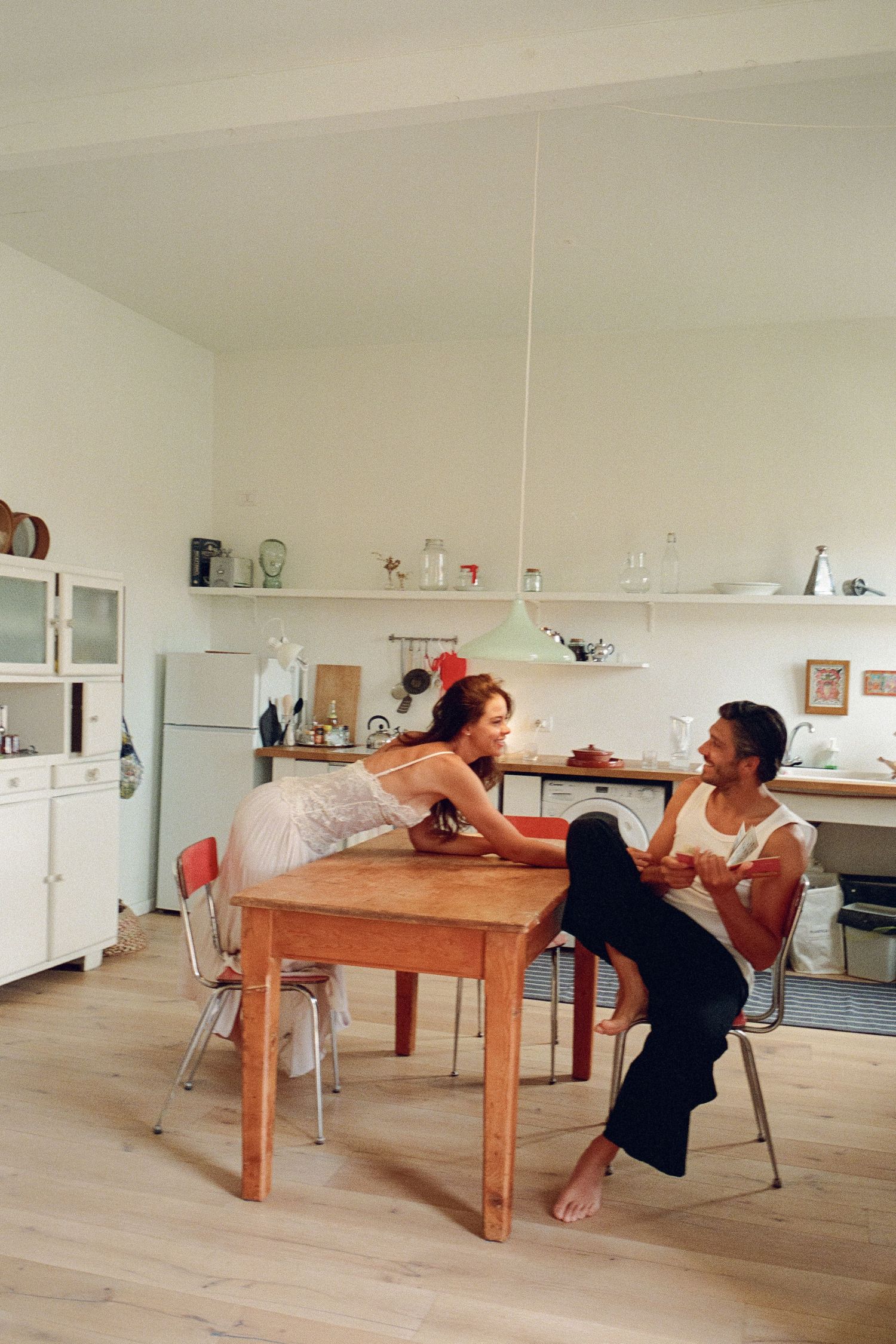 Couple sharing an intimate conversation at a wooden kitchen table in a bright, modern apartment.