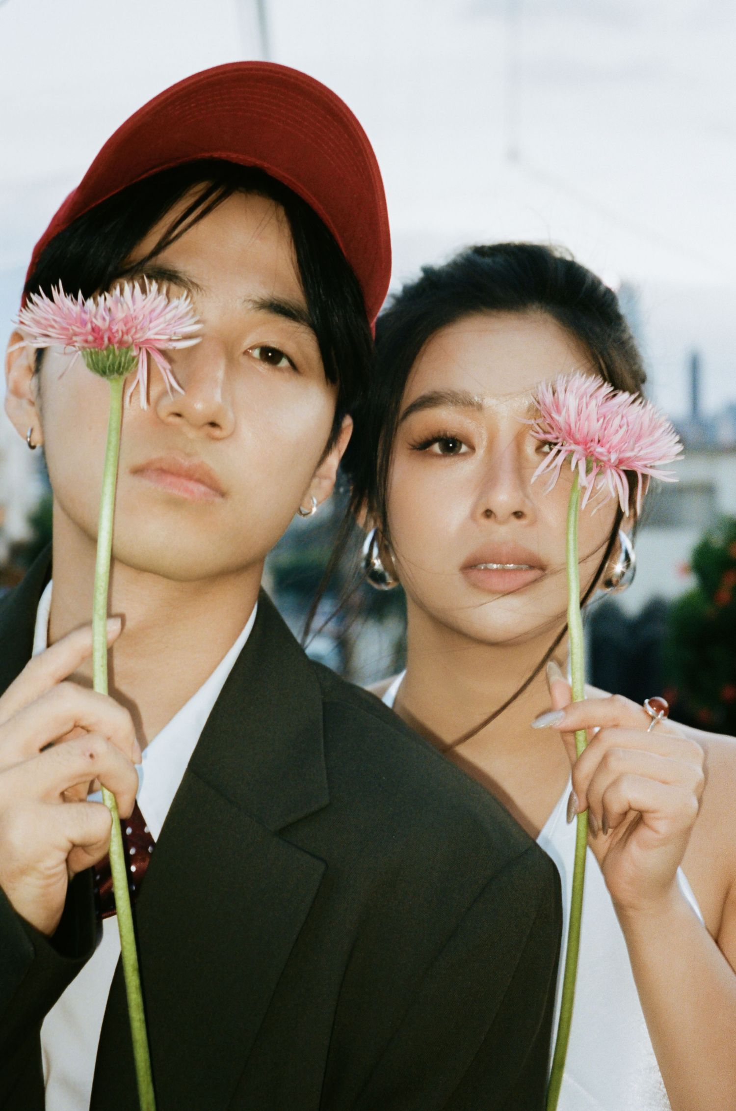 Asian couple holding pink flowers in front of their faces outdoors.