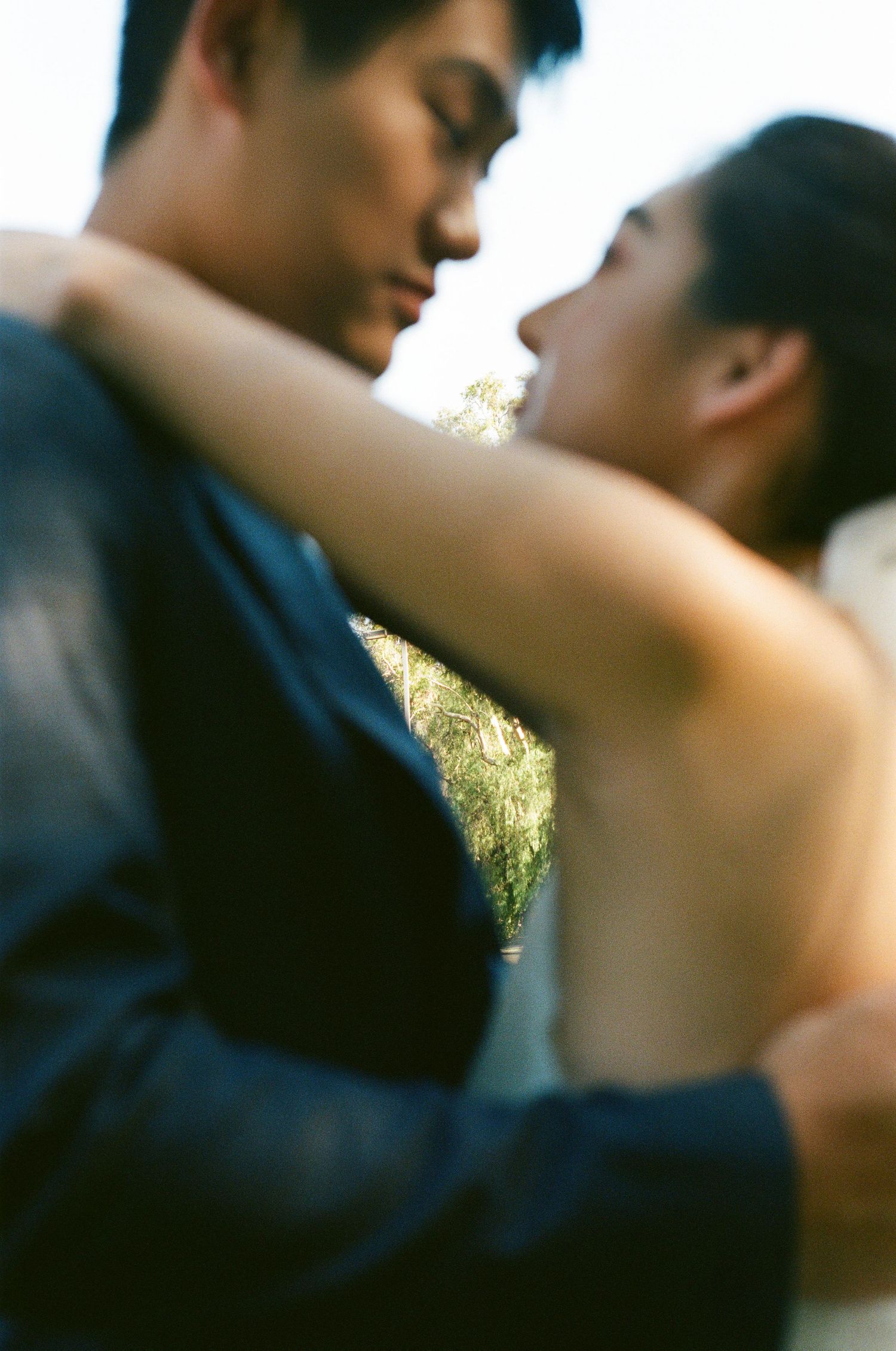 Bride embraces groom outdoors in a tender close-up wedding portrait with soft bokeh.