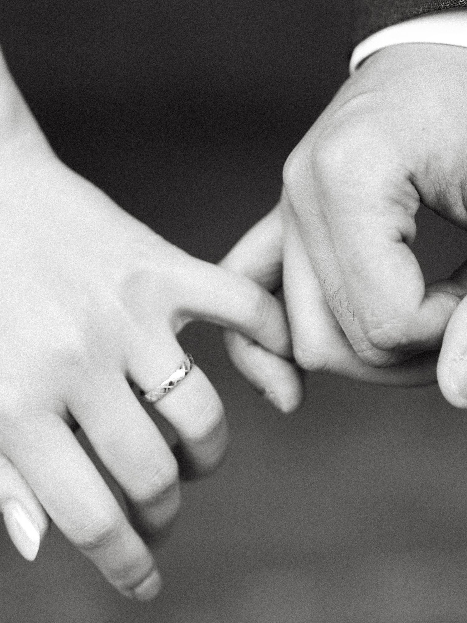 Black and white close-up of newlyweds linking pinkies, highlighting the bride's elegant wedding band.