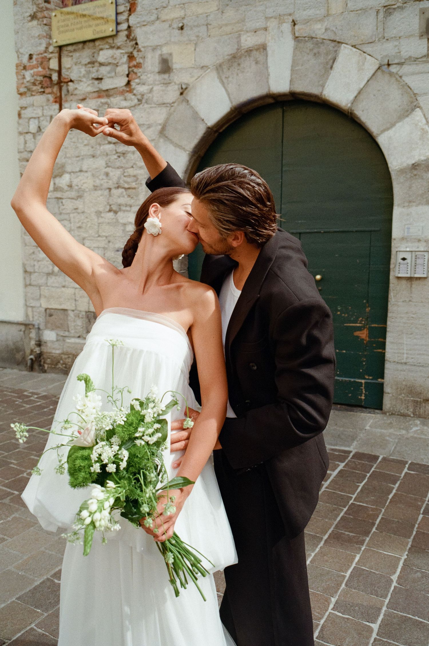 Bride and groom sharing a kiss while she raises her arm gracefully holding a white bouquet.