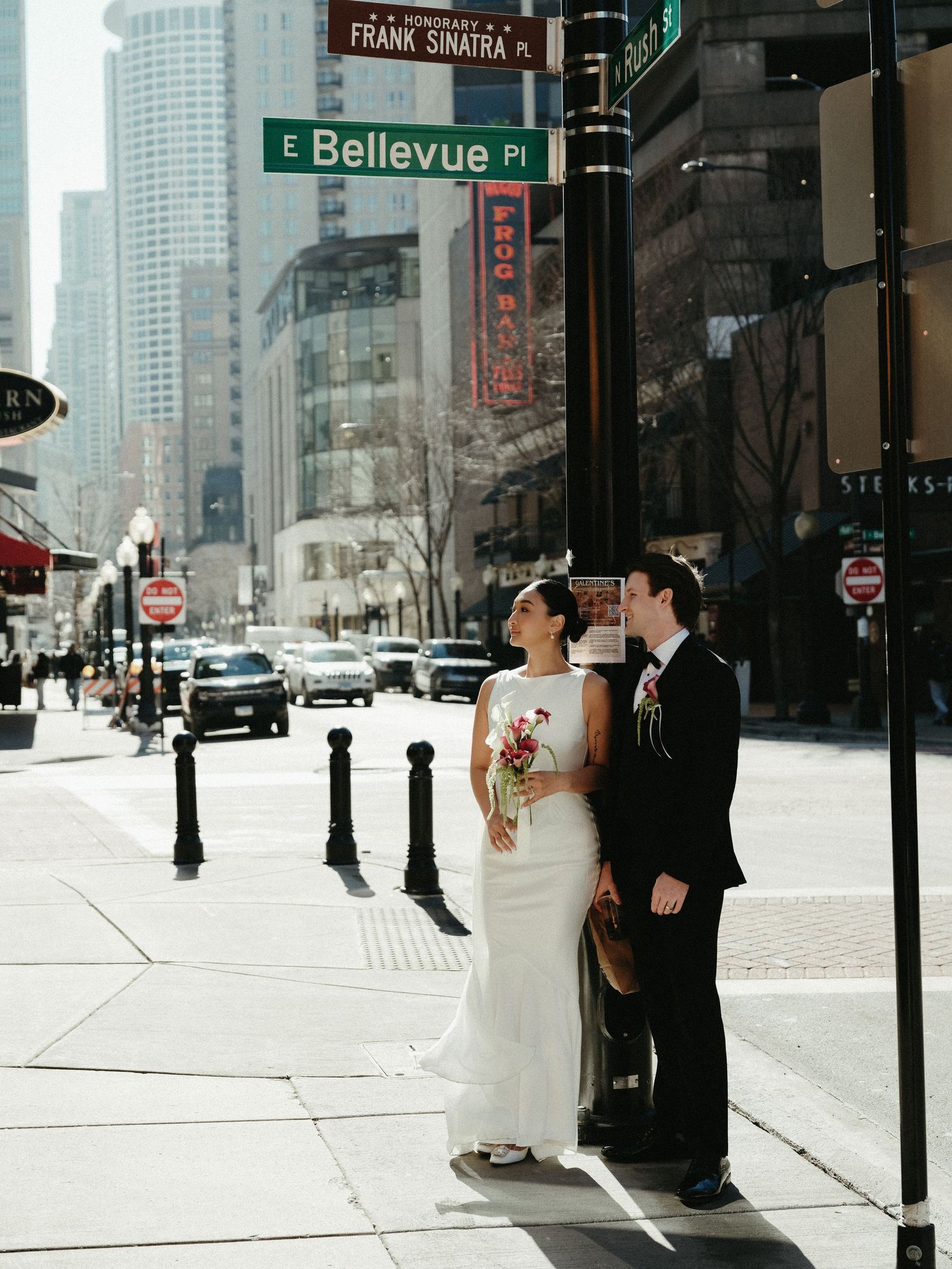 Couple poses under Frank Sinatra Place and E Bellevue Pl street signs in Chicago on their wedding day.
