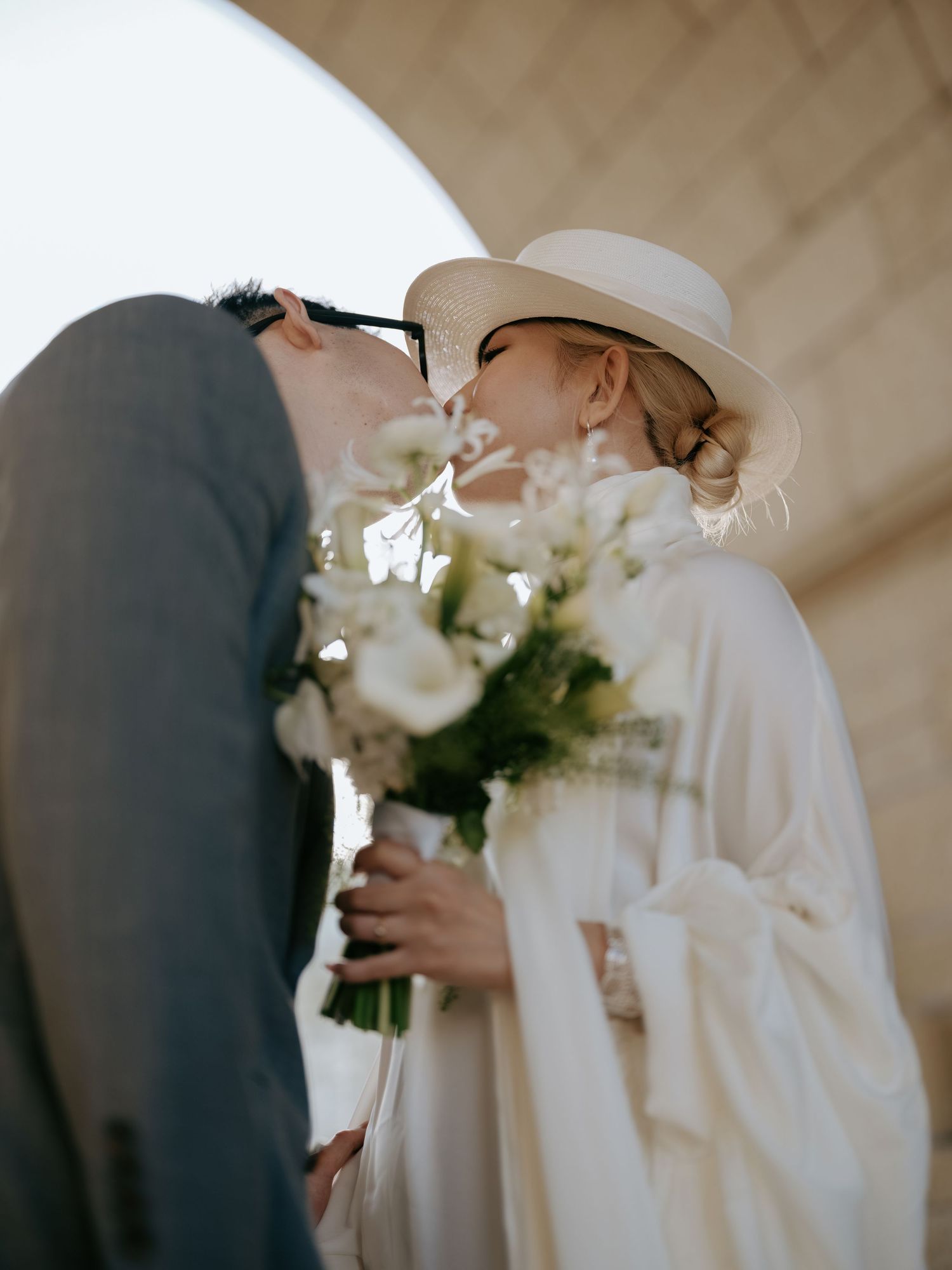 Bride and groom share a romantic kiss under an archway, bride holding white bouquet.