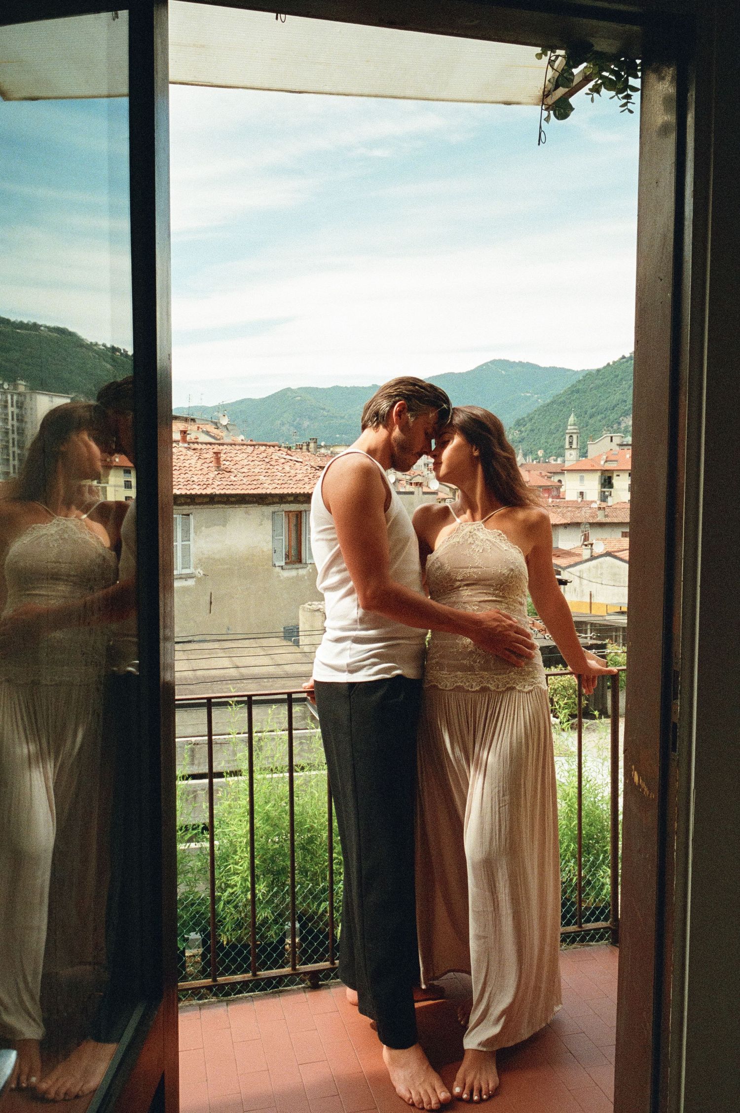 Couple sharing an intimate moment on a balcony with stunning Italian mountain town backdrop.