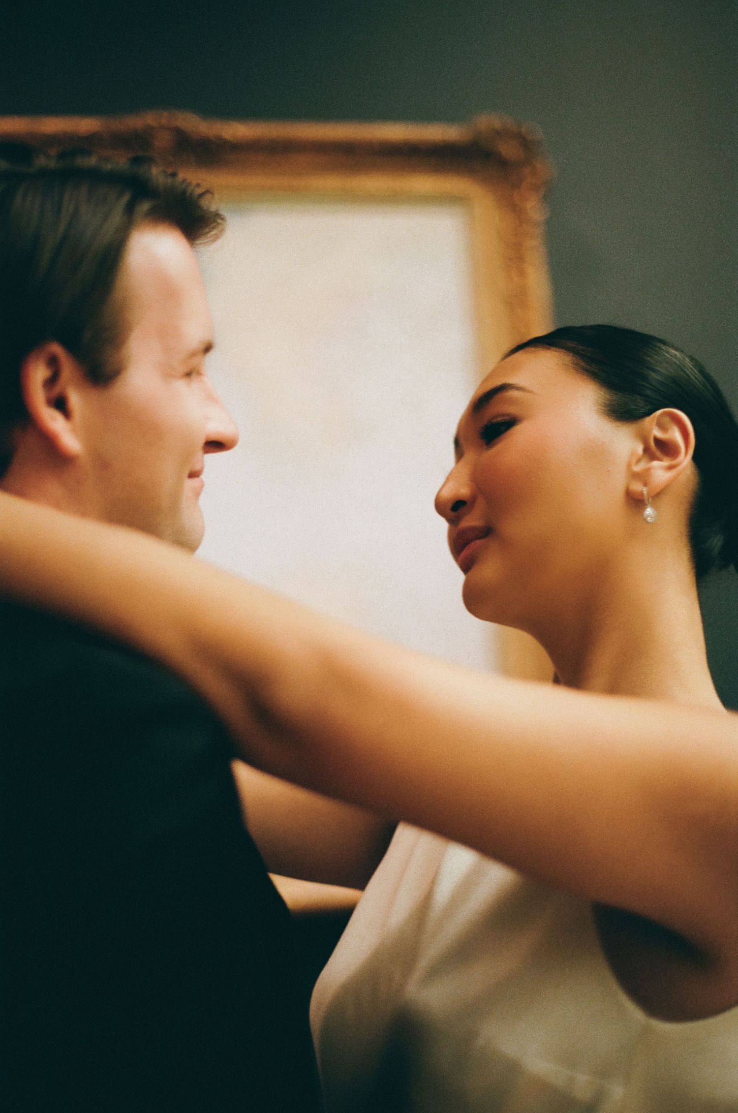 Bride and groom share an intimate dance moment, gazing into each other's eyes near a gold-framed painting.