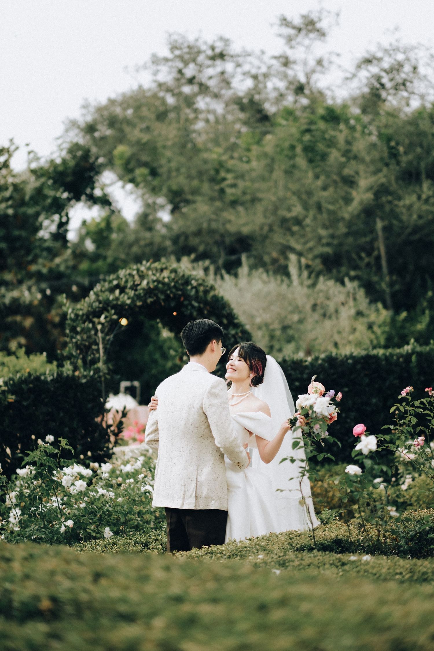 Bride and groom sharing a joyful moment in a lush garden surrounded by blooming roses.