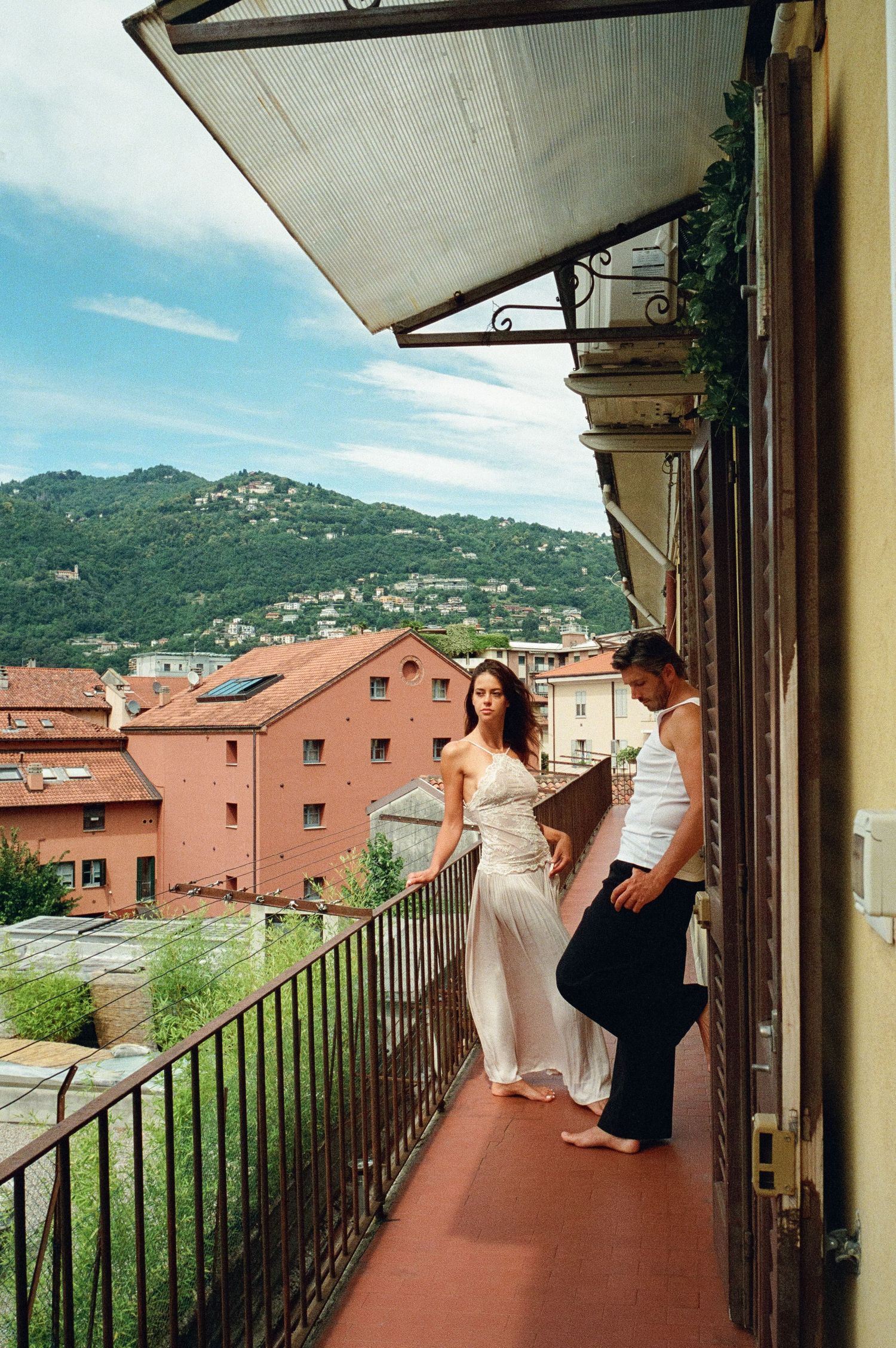 Couple strolling on a charming Italian balcony with panoramic views of hillside architecture.