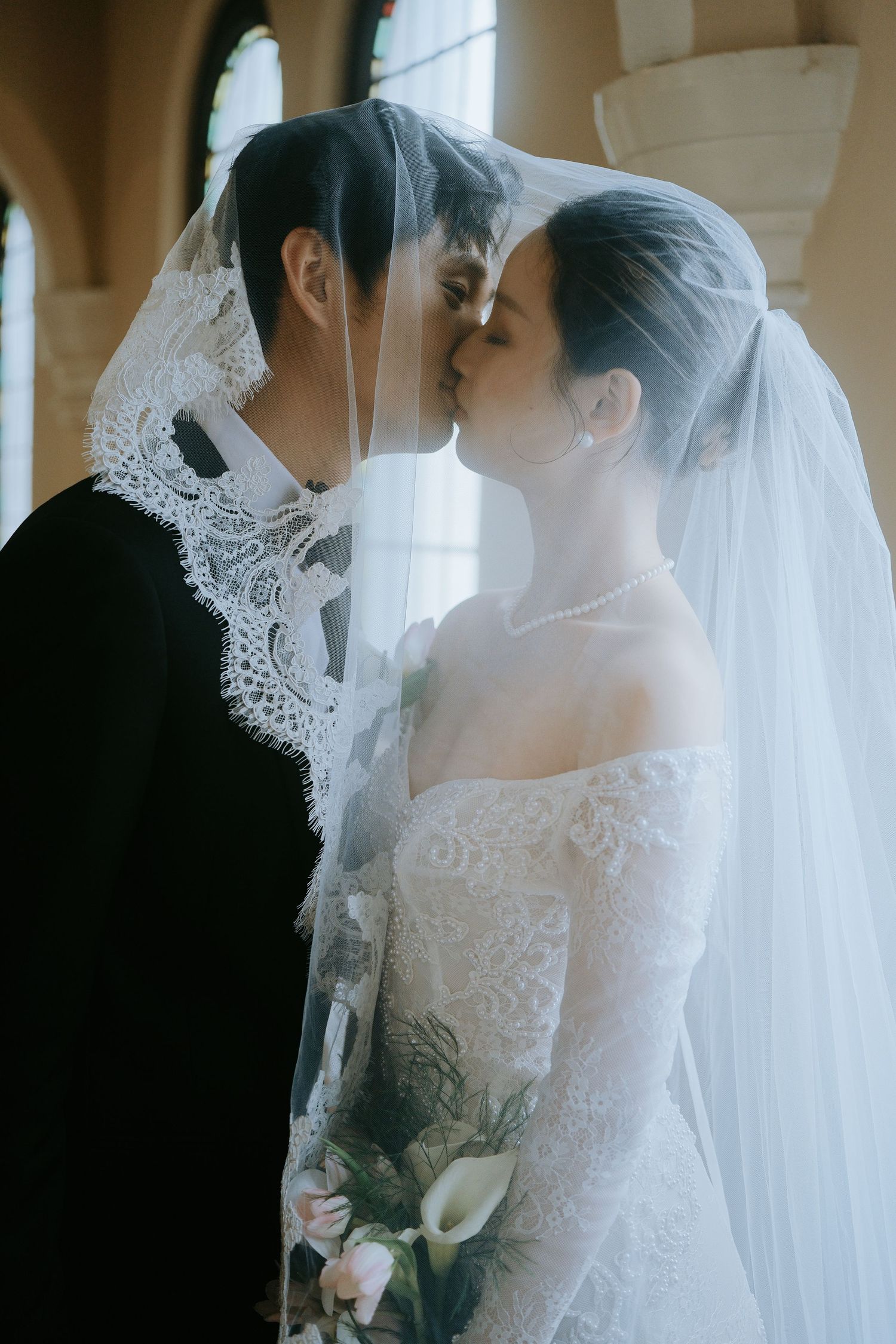 Bride and groom share a romantic kiss beneath the brides lace veil in church.