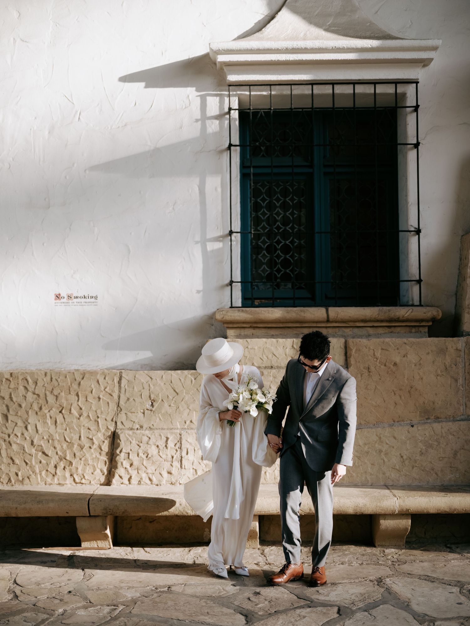 Bride and groom hold hands walking on cobblestone path beside white historic building.