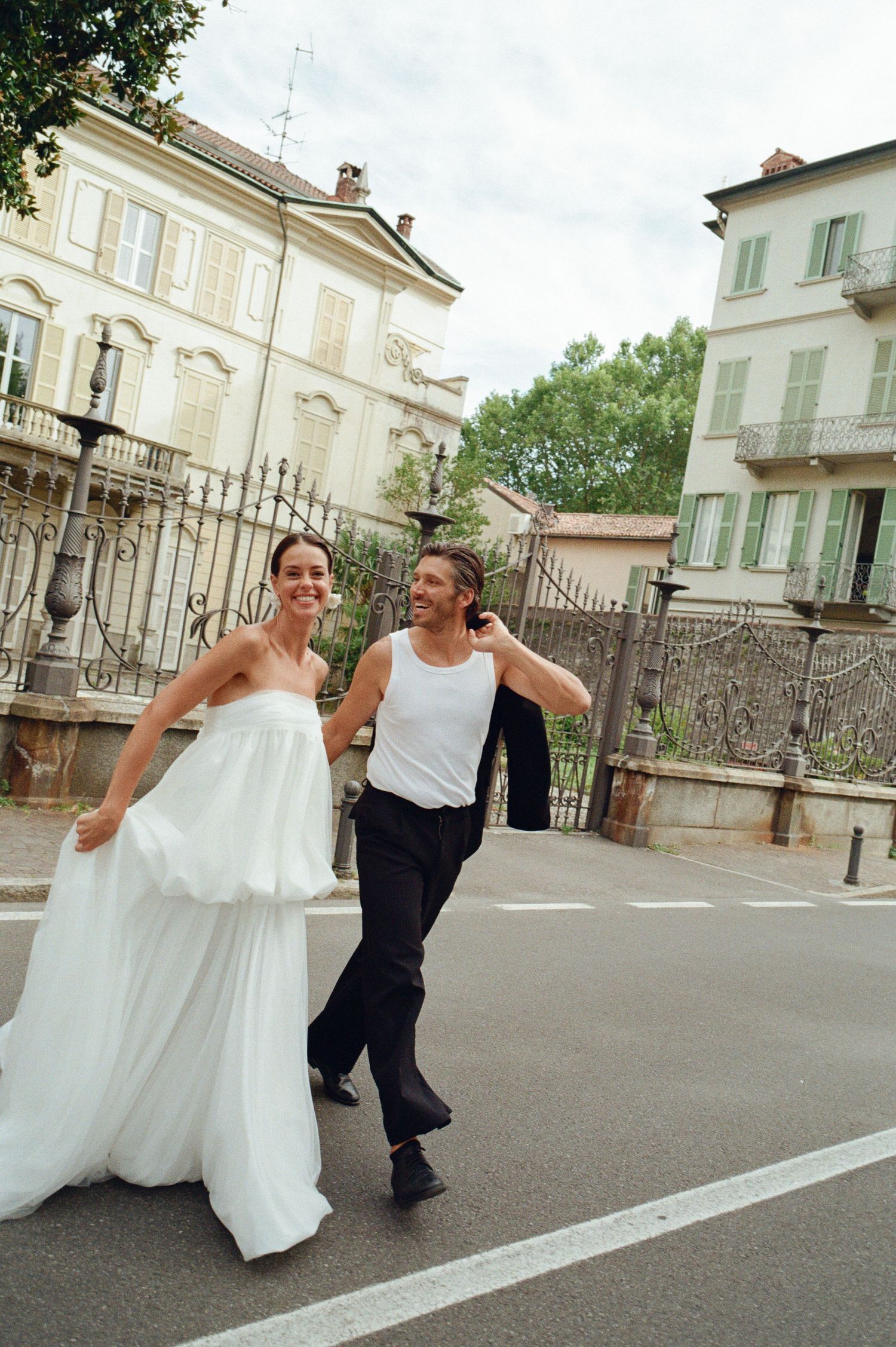 Joyful bride and groom in casual attire walk and laugh together on Italian street.