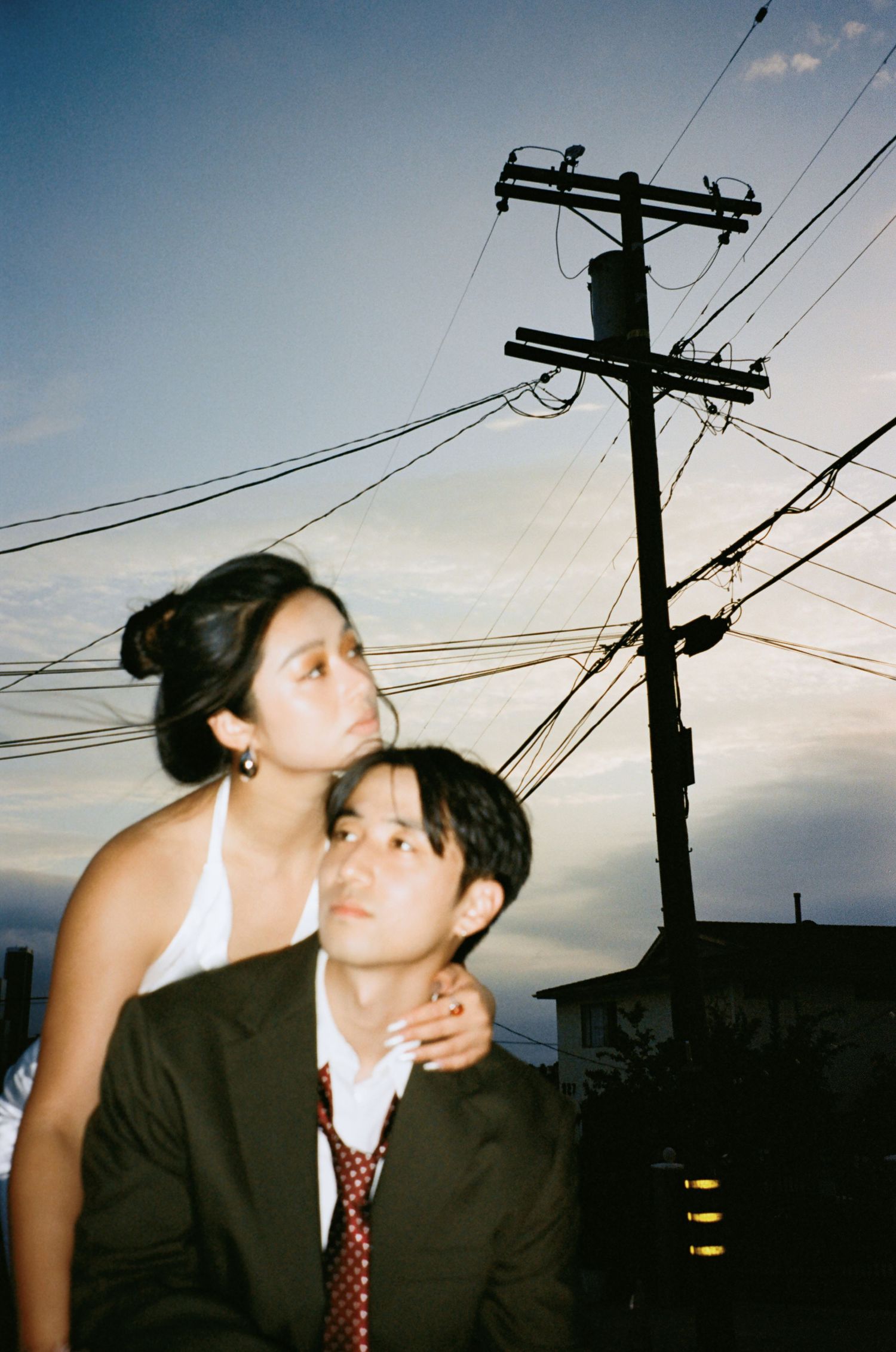 Couple in wedding attire pose under utility pole at dusk, bride in white rests hands on groom's shoulders.
