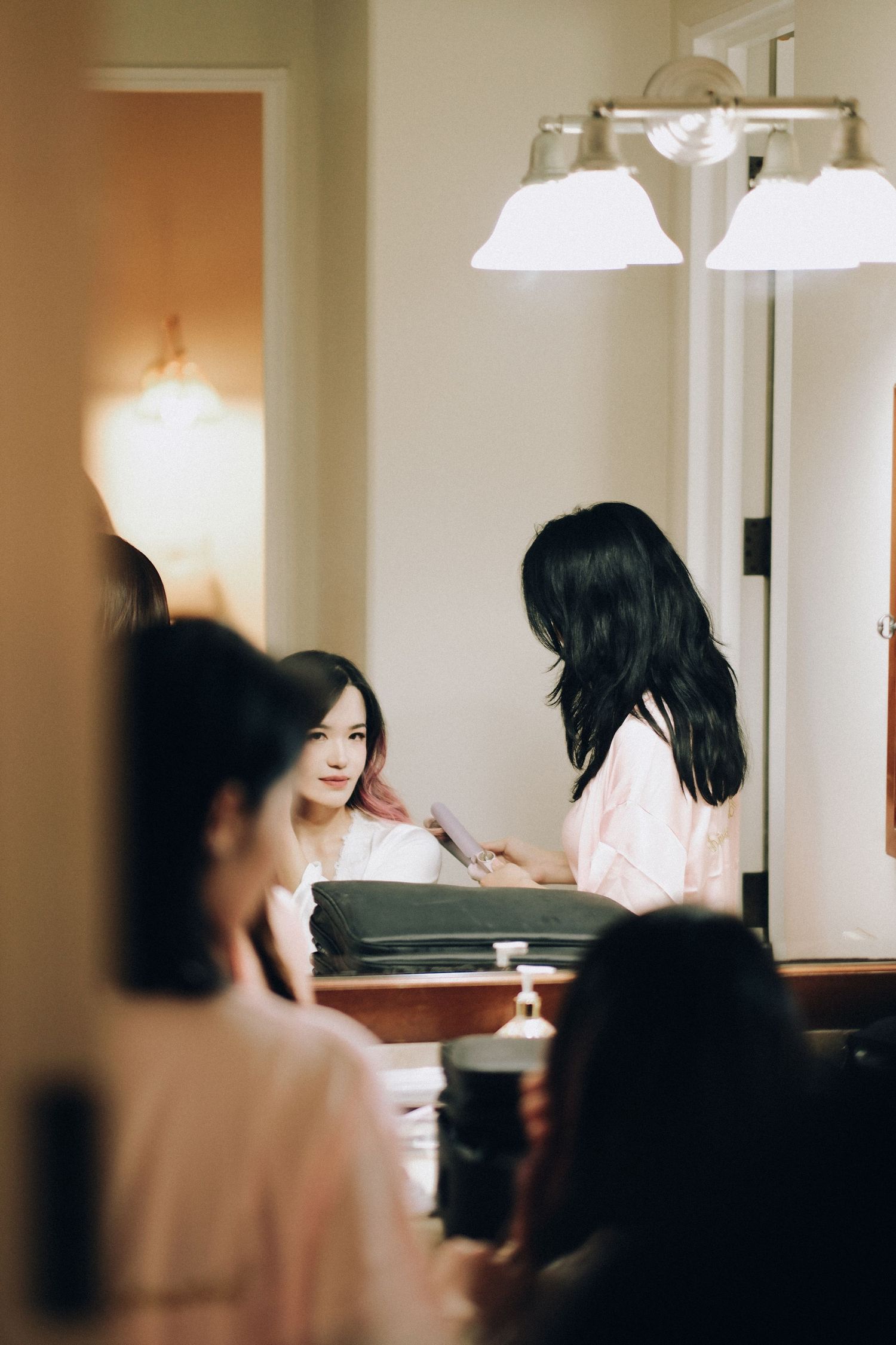 Bride smiling in mirror reflection during wedding morning preparations with bridesmaids.