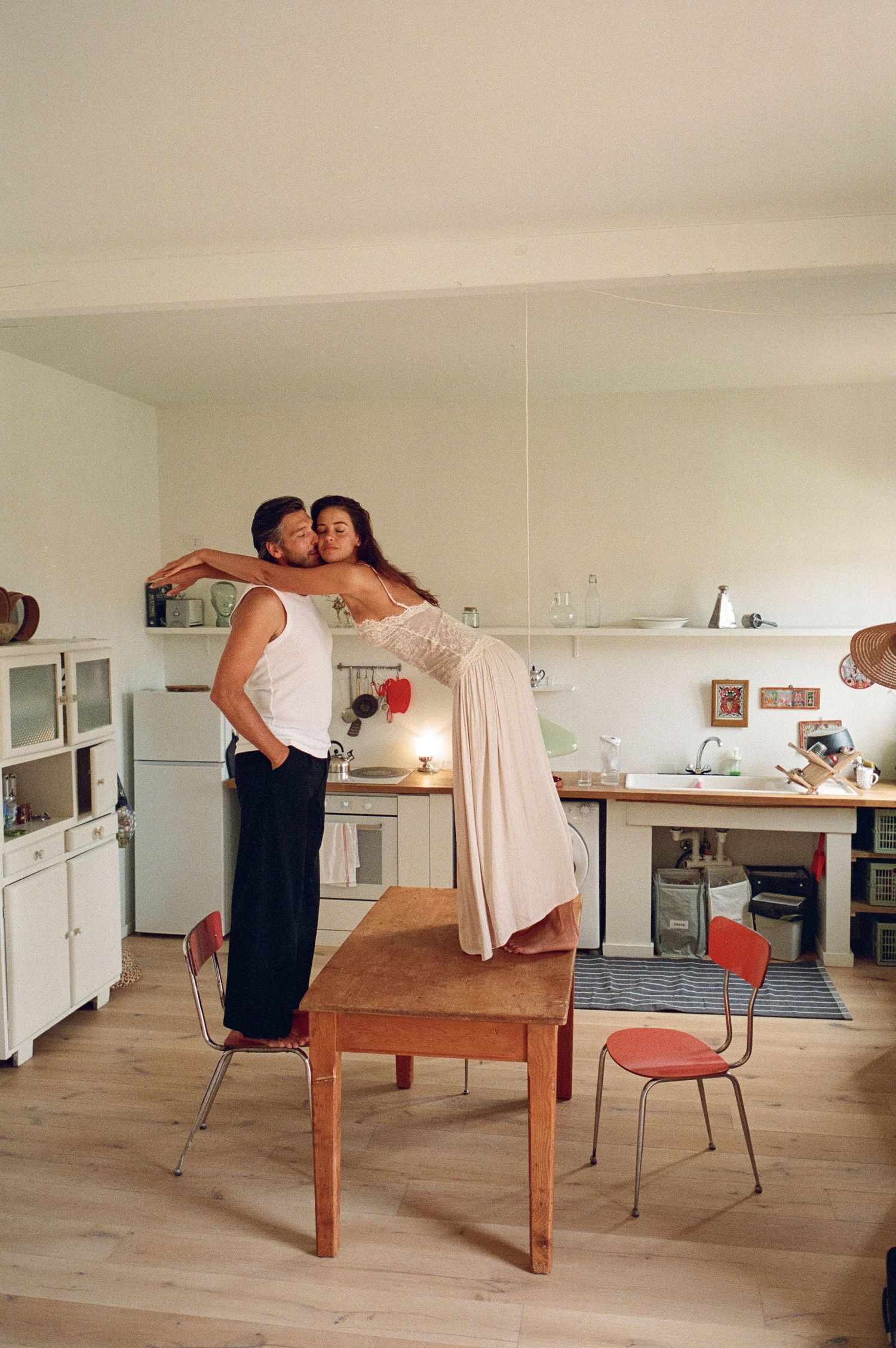 Romantic couple embracing in a bright kitchen, woman standing on table kissing man tenderly.