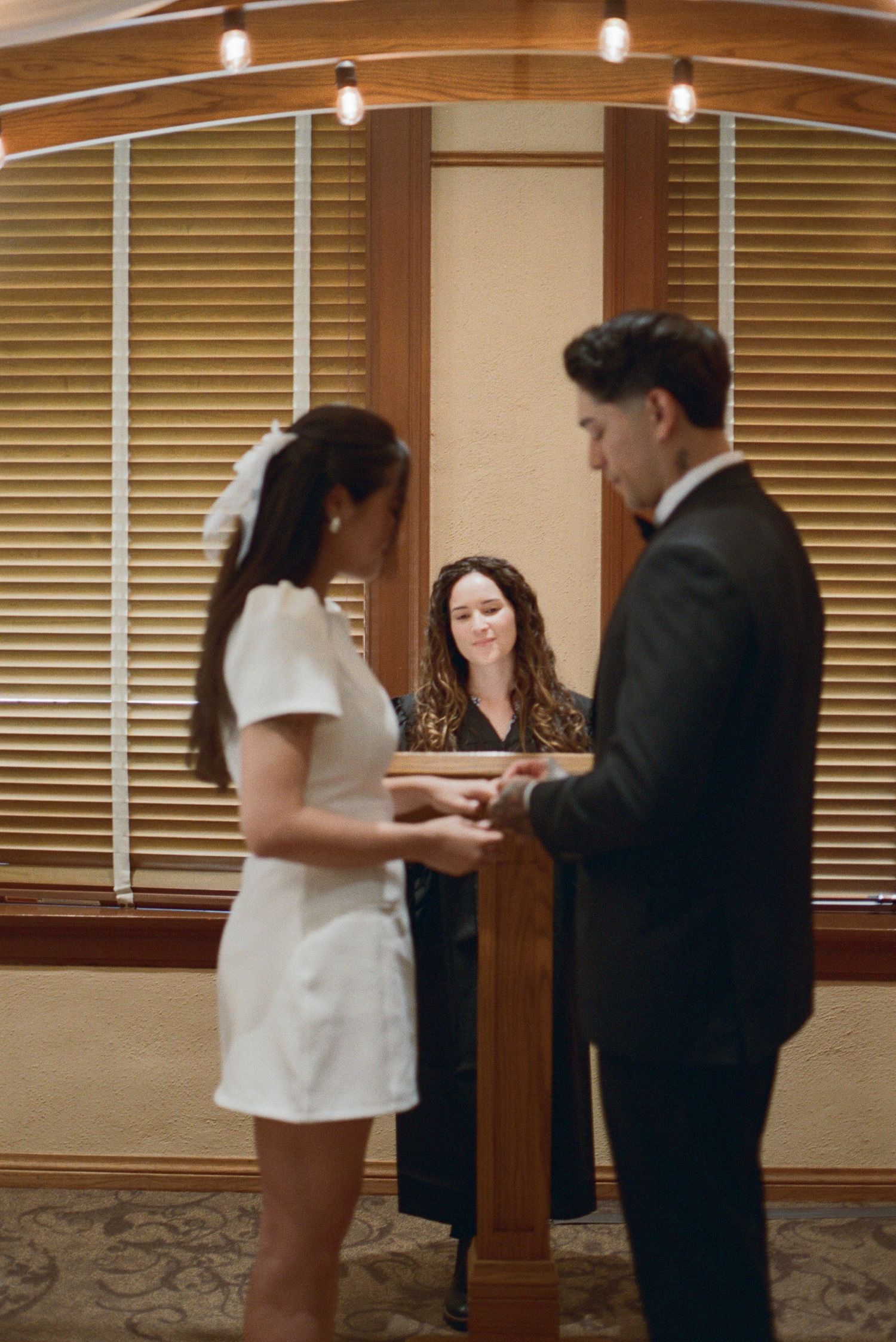 Bride and groom exchange vows before smiling officiant at elegant indoor wedding ceremony.