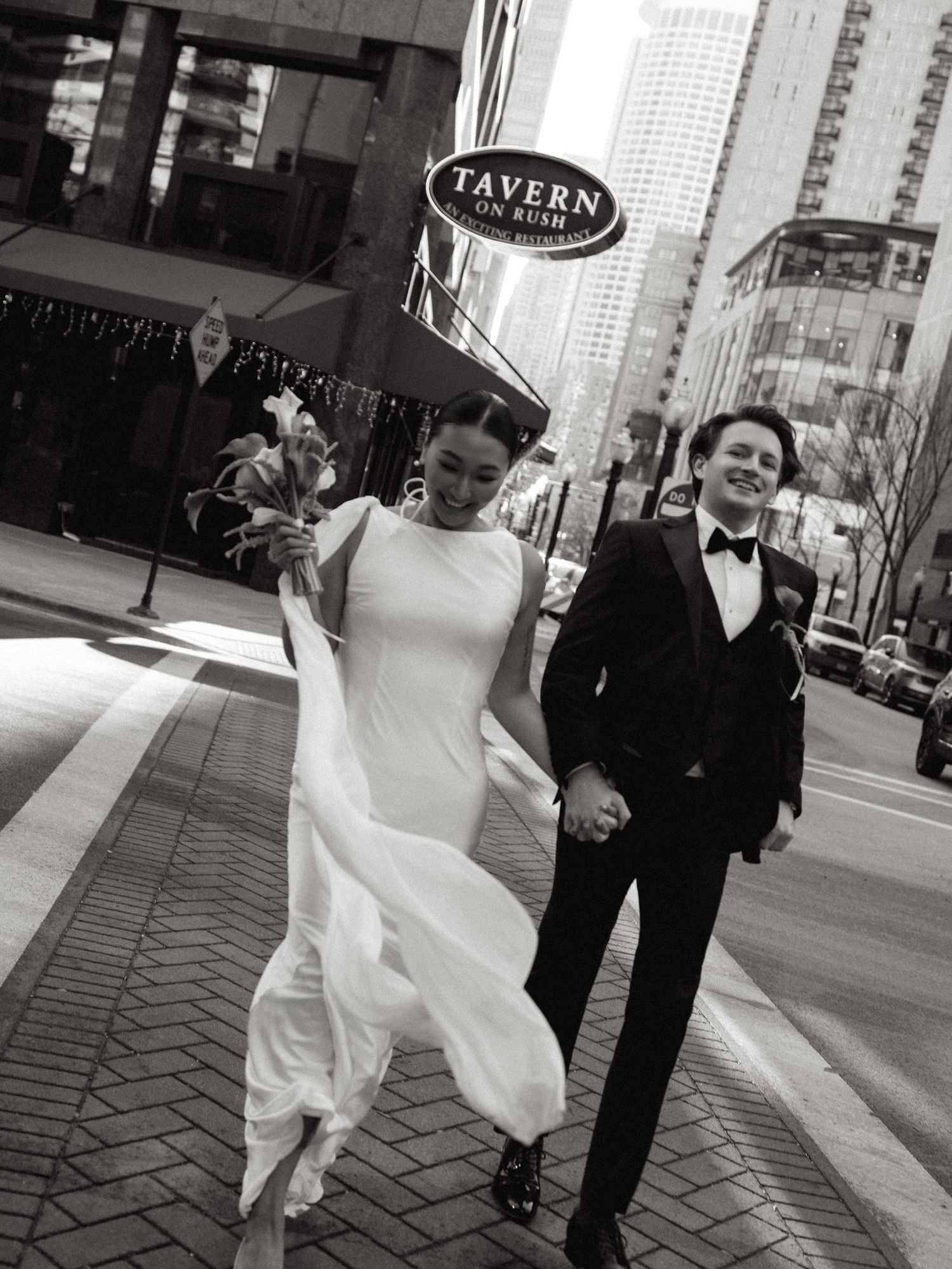 Black and white photo of bride and groom holding hands crossing a Chicago street near Tavern on Rush.