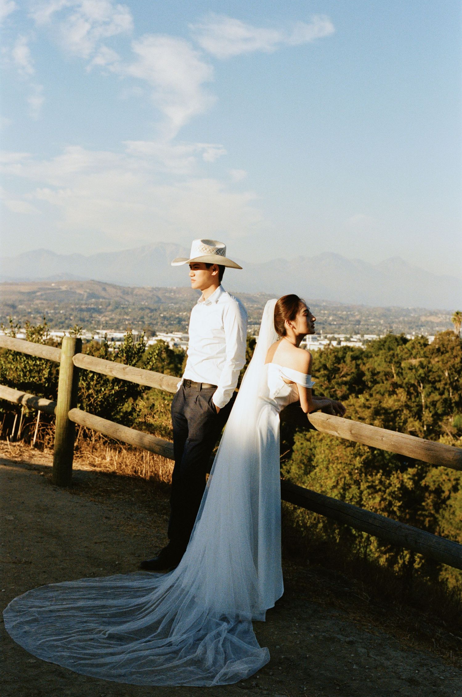 Wedding couple standing by a rustic fence with a breathtaking mountain panorama behind them.