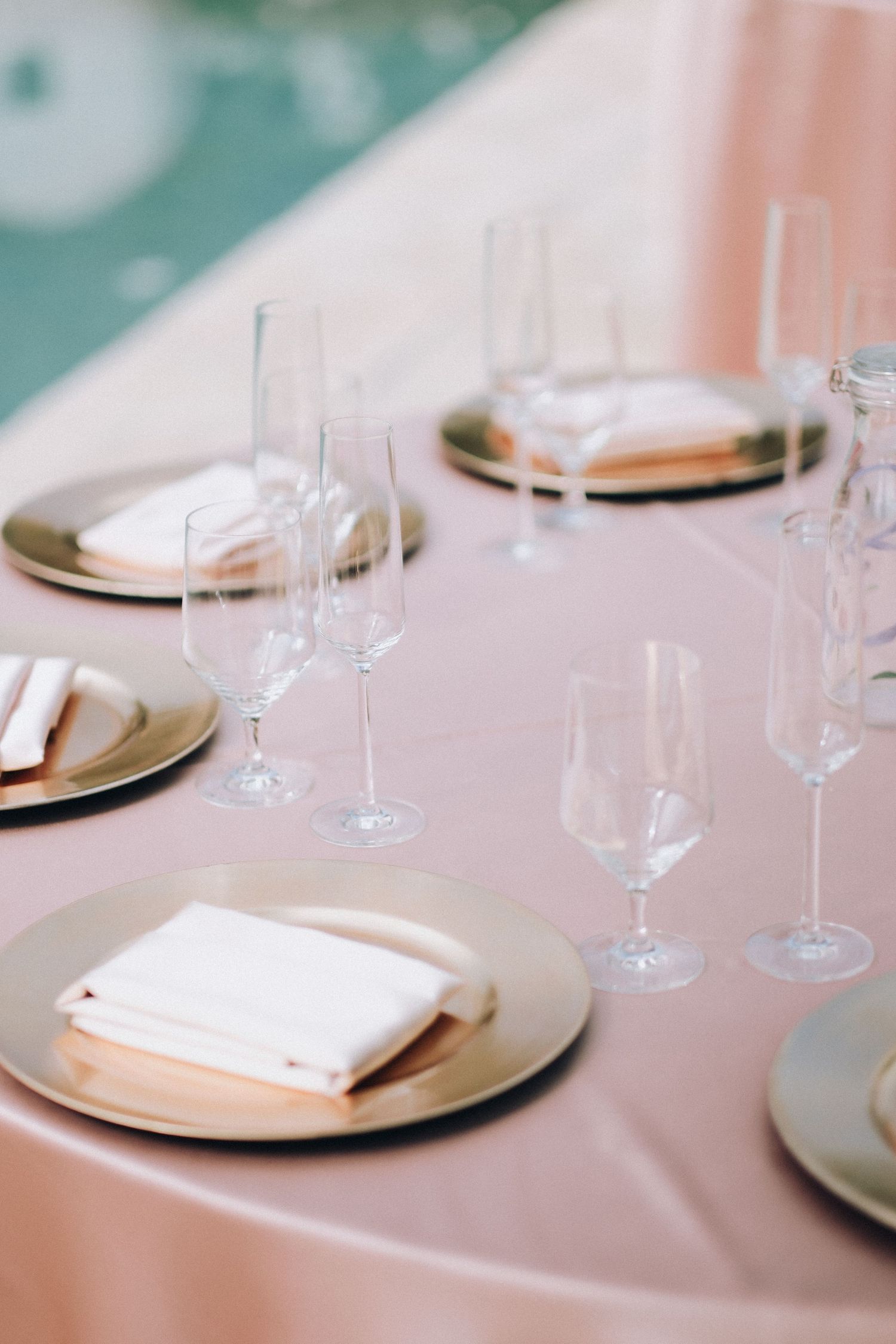 Elegant pink wedding reception table with gold charger plates and crystal glassware.