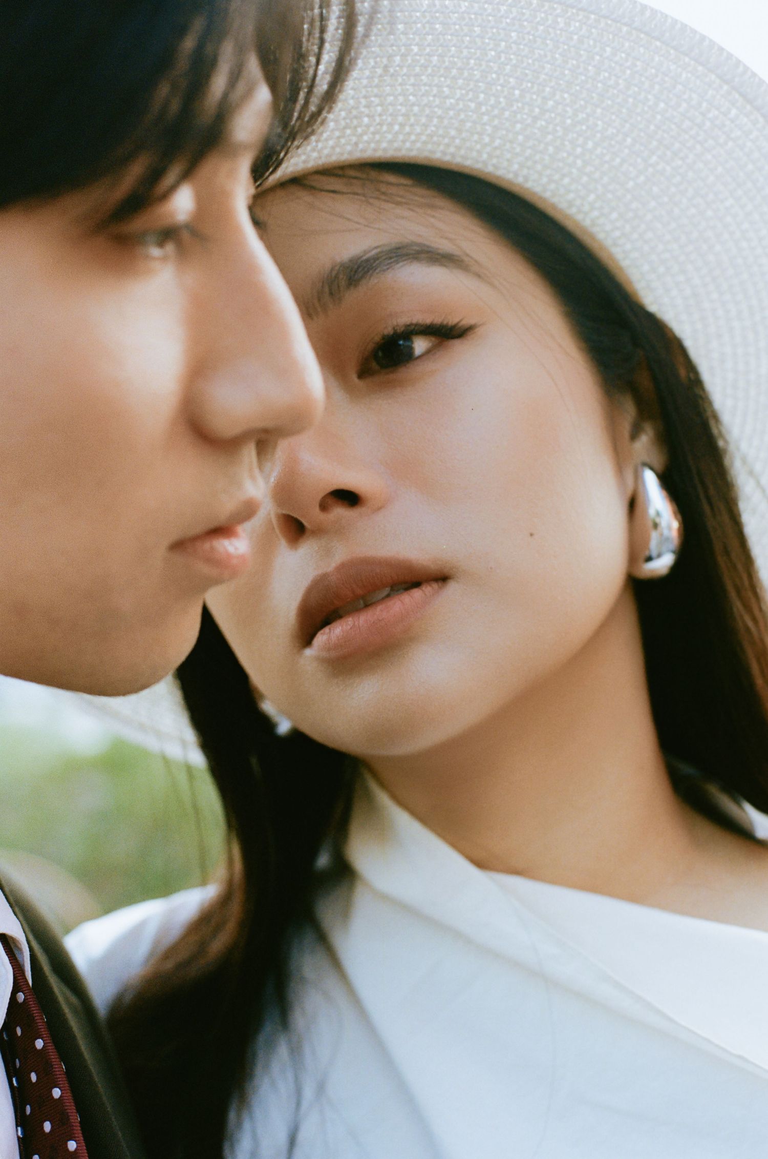 Close-up portrait of bride in white hat and groom leaning in, captured in soft natural light.