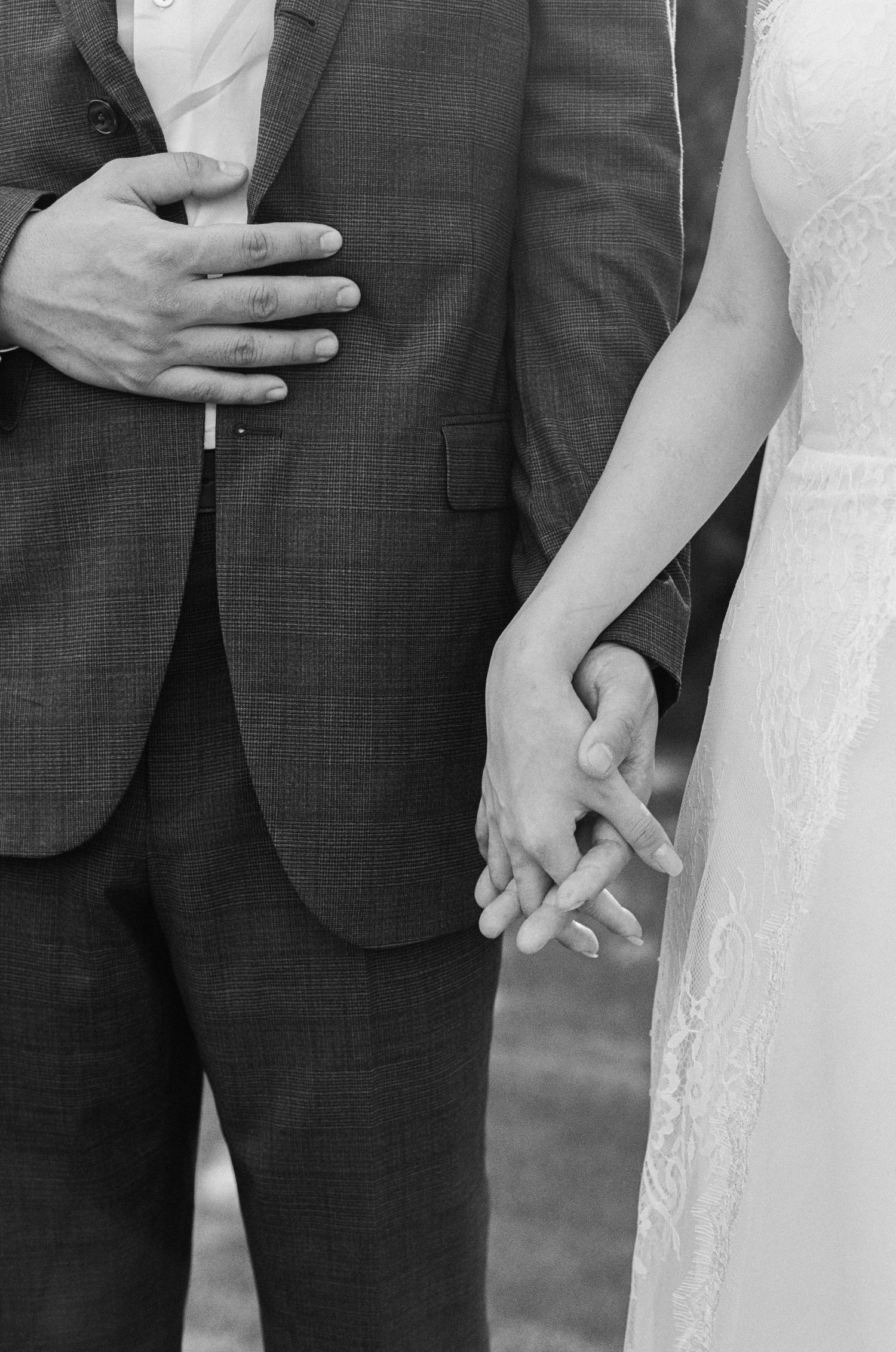 Black and white photo of bride and groom holding hands in wedding attire outdoors.