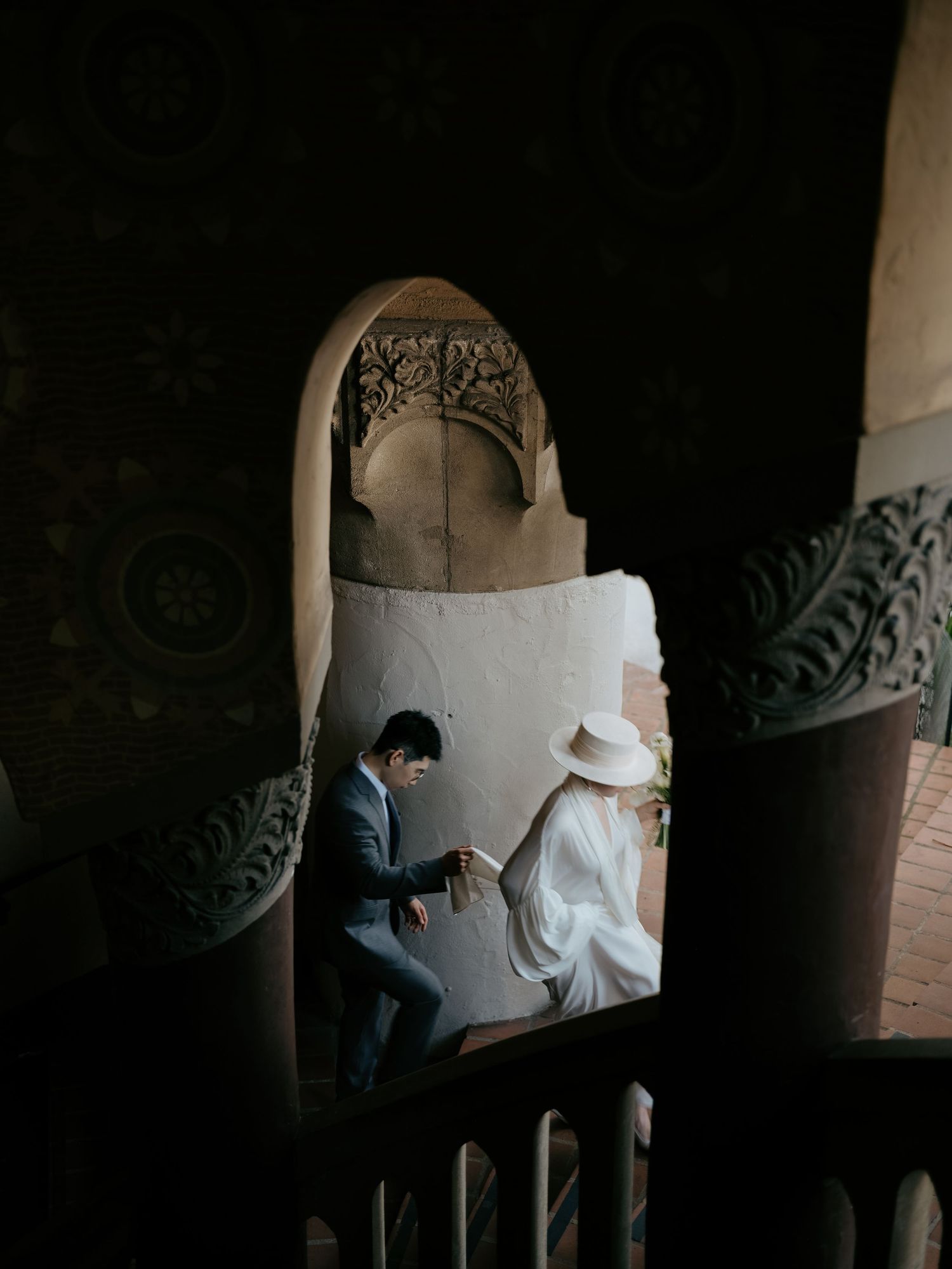 Bride and groom sit intimately together framed by ornate Moorish archway in dim light.
