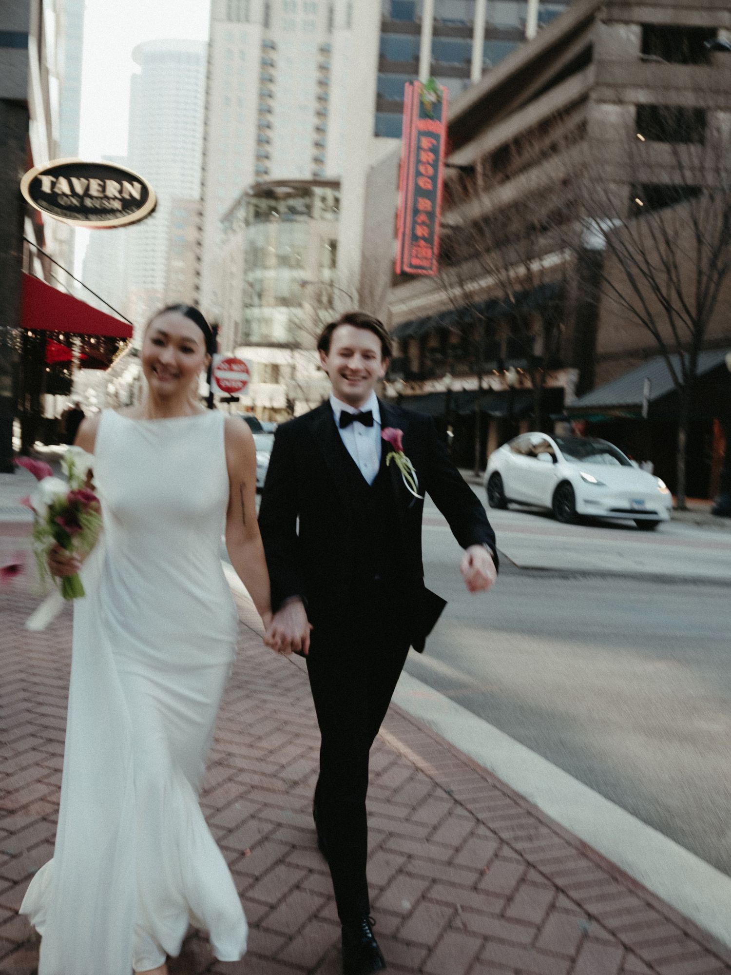 Bride and groom holding hands walking across a brick street in downtown city on their wedding day.