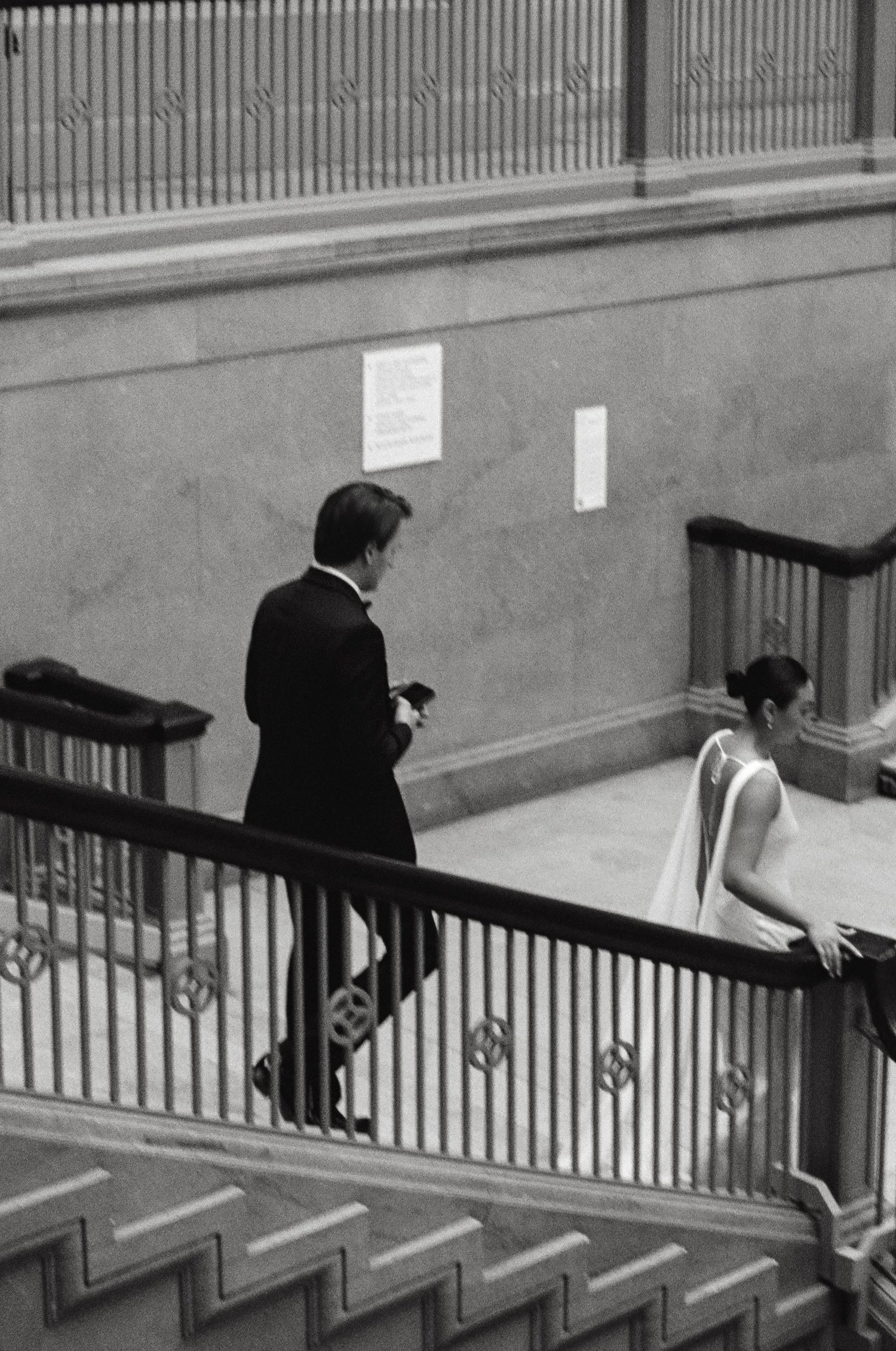 Black and white photo of a bride and groom descending a grand staircase inside an elegant museum.