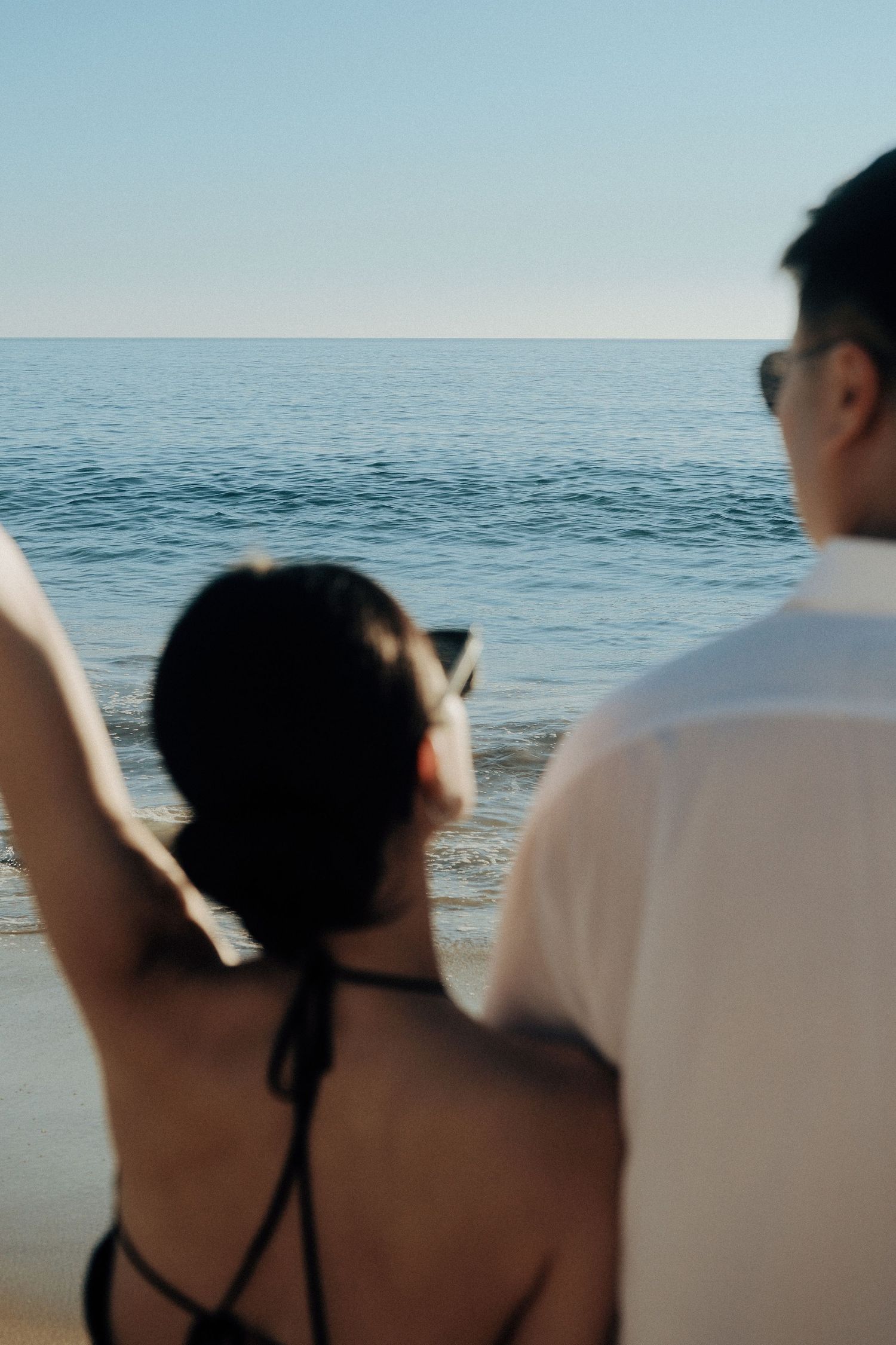 Couple standing on beach photographing ocean horizon on a clear sunny day.