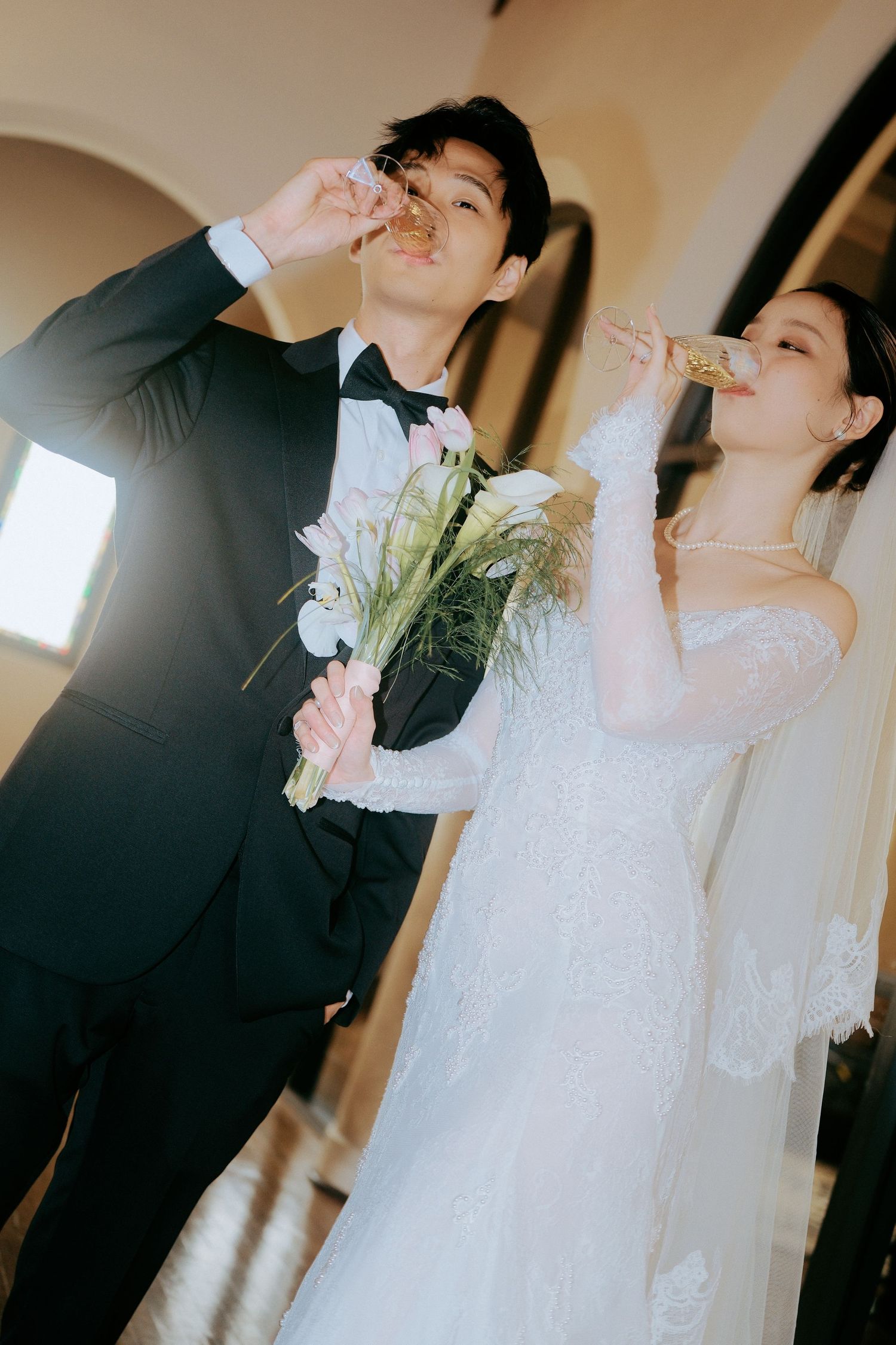 Wedding couple toasting with champagne glasses while bride holds a floral bouquet.