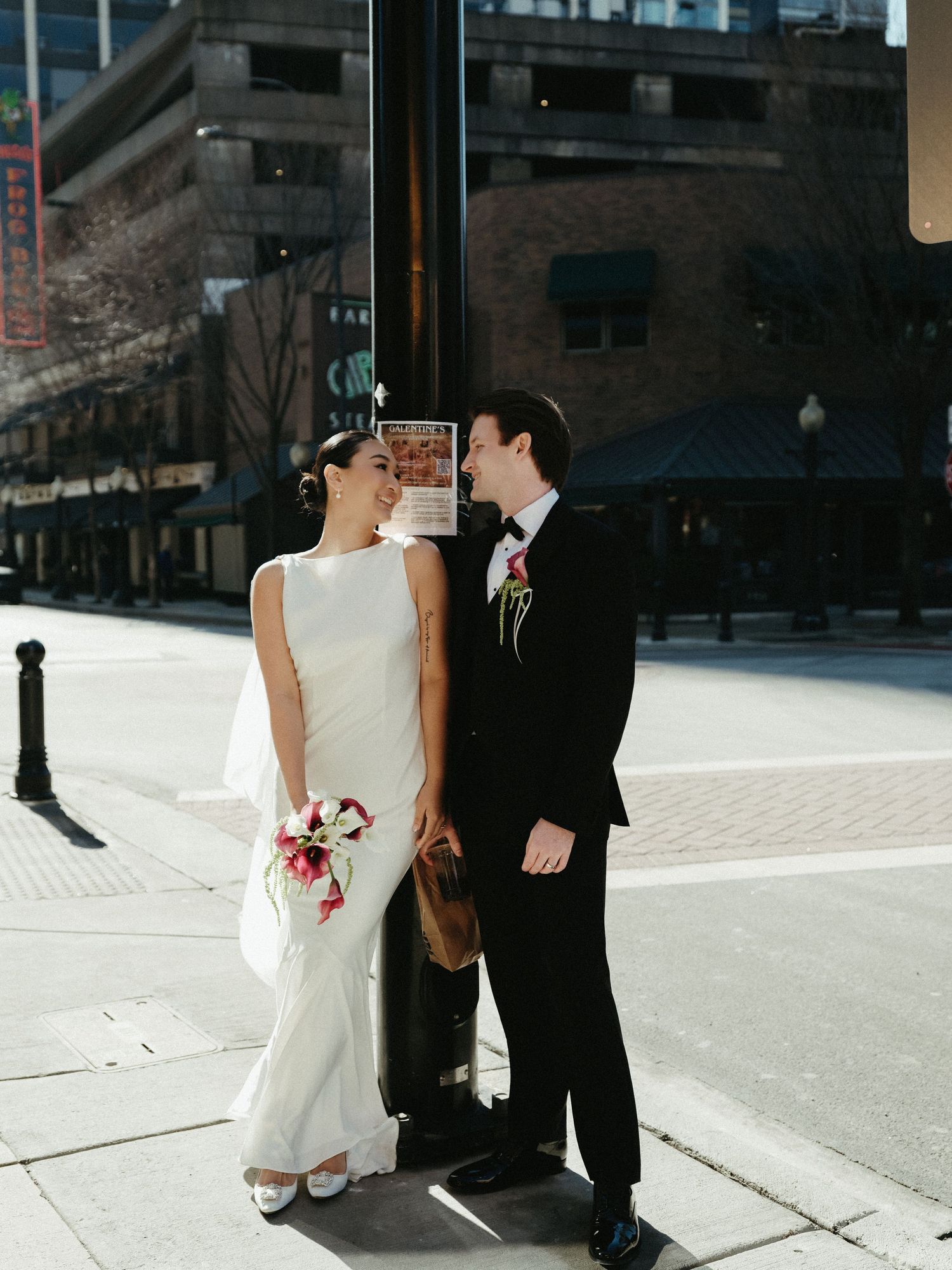 Bride and groom laugh together leaning against a street pole in an urban Chicago setting.