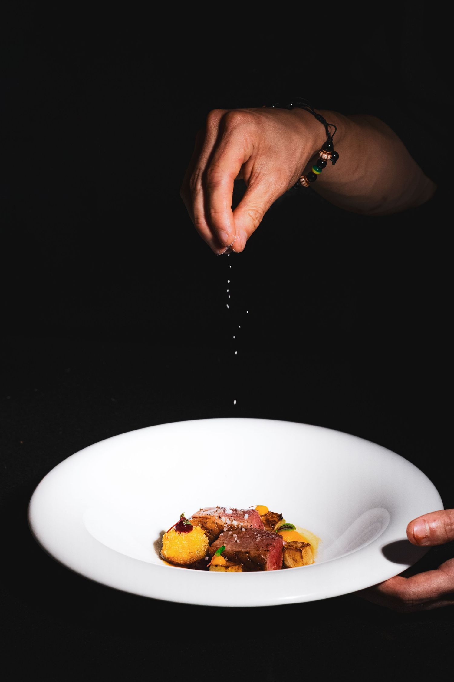 Food photography for tasting menu, clean style, hand sprinkling salt onto steak