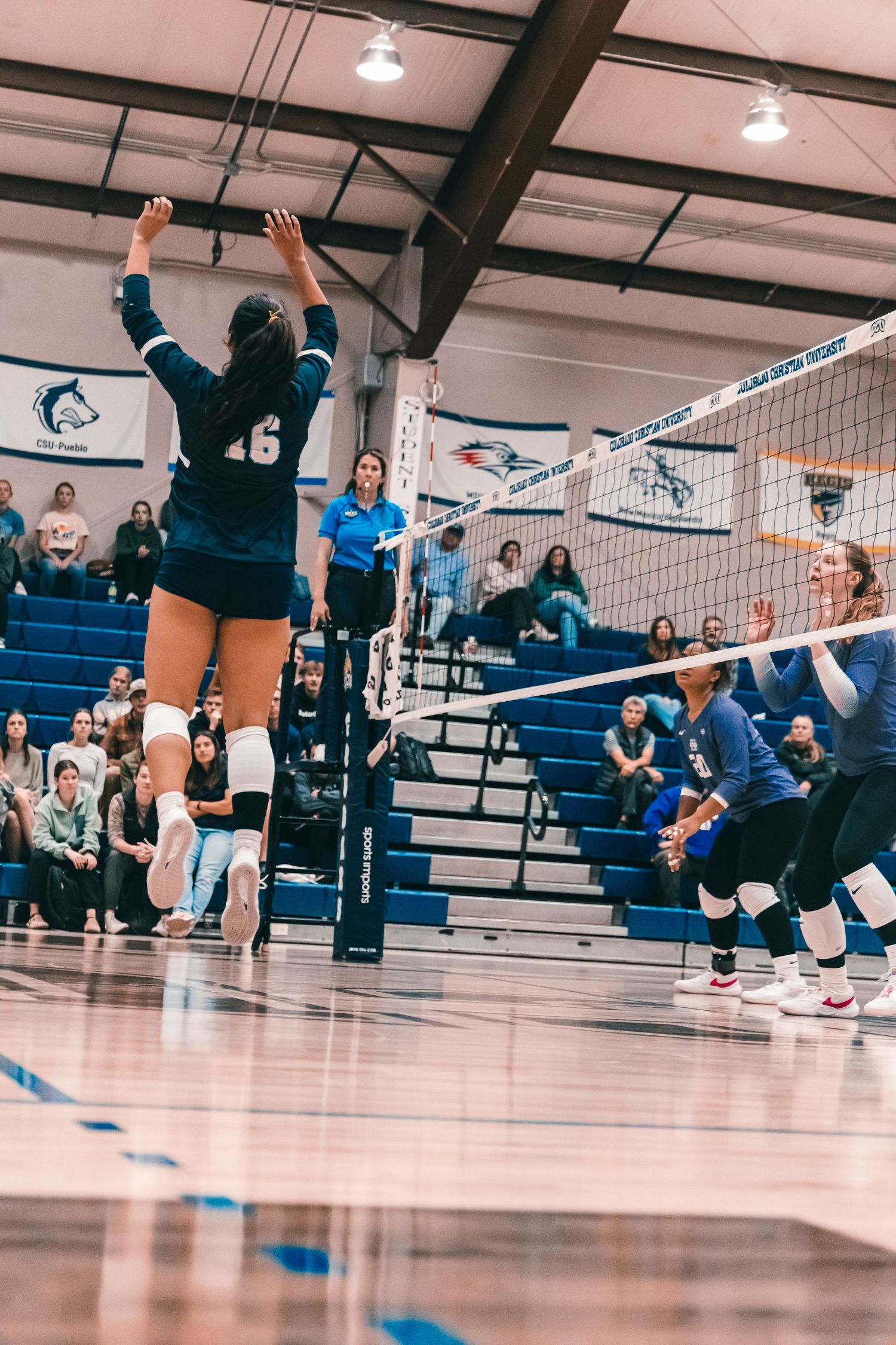Colorado Christian University volleyball player #16 jumping near the net with opposing defenders reacting