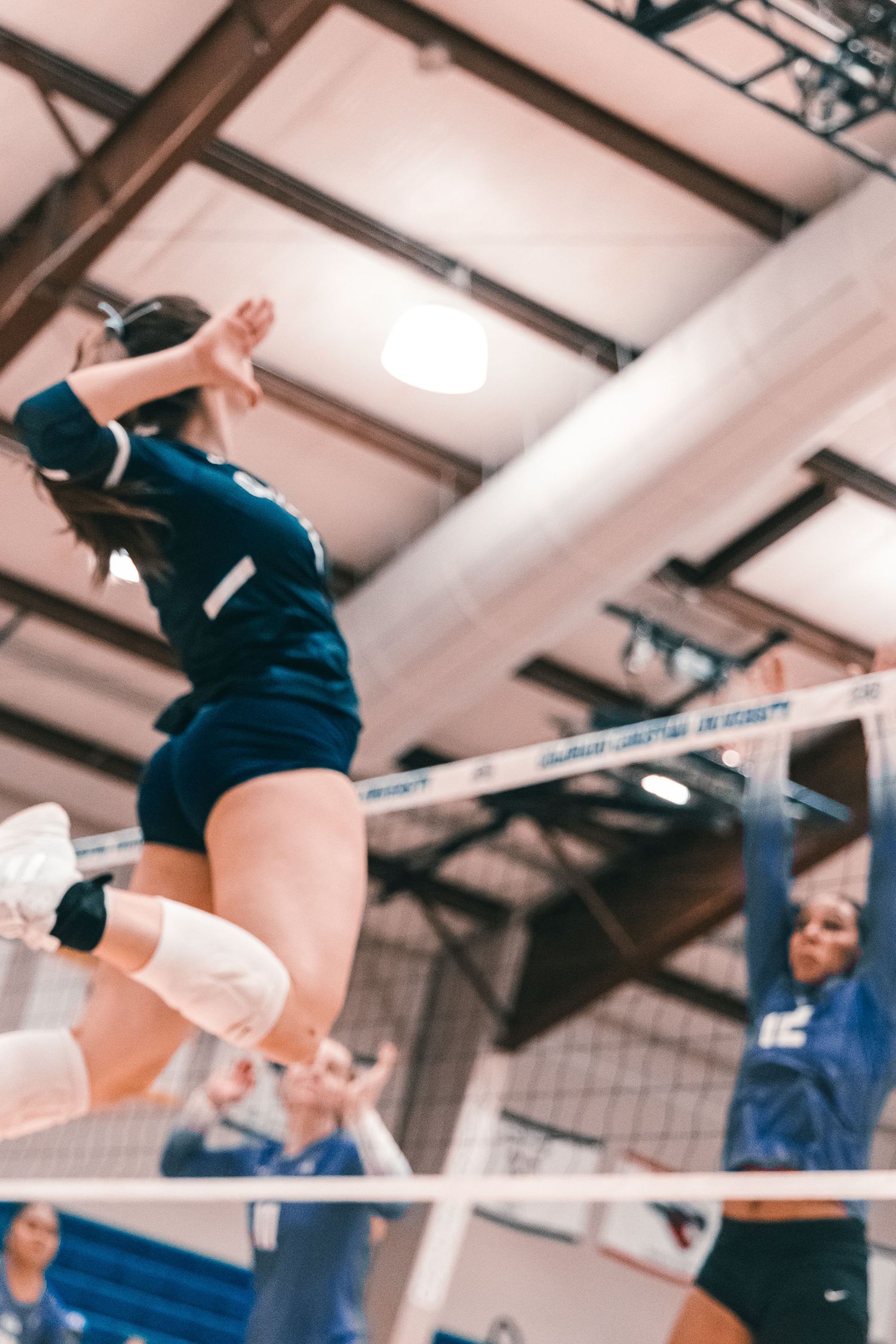 Low-angle action shot of Colorado Christian University volleyball player jumping at the net against opponent #12