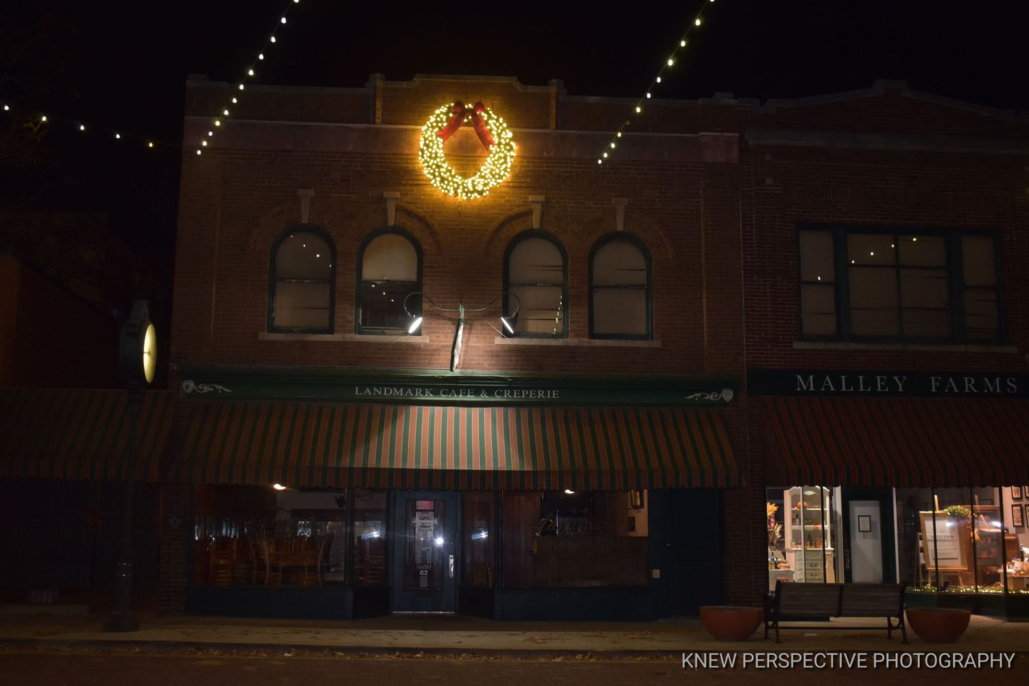 String lights and illuminated wreath create a warm ambiance in a dark storefront setting at night.