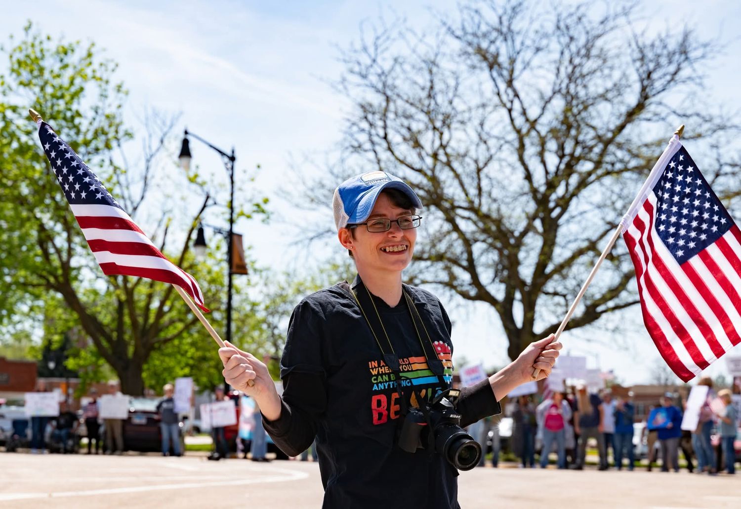 A protest photographer features American flags waving in the breeze as participants demonstrate along a small town street.