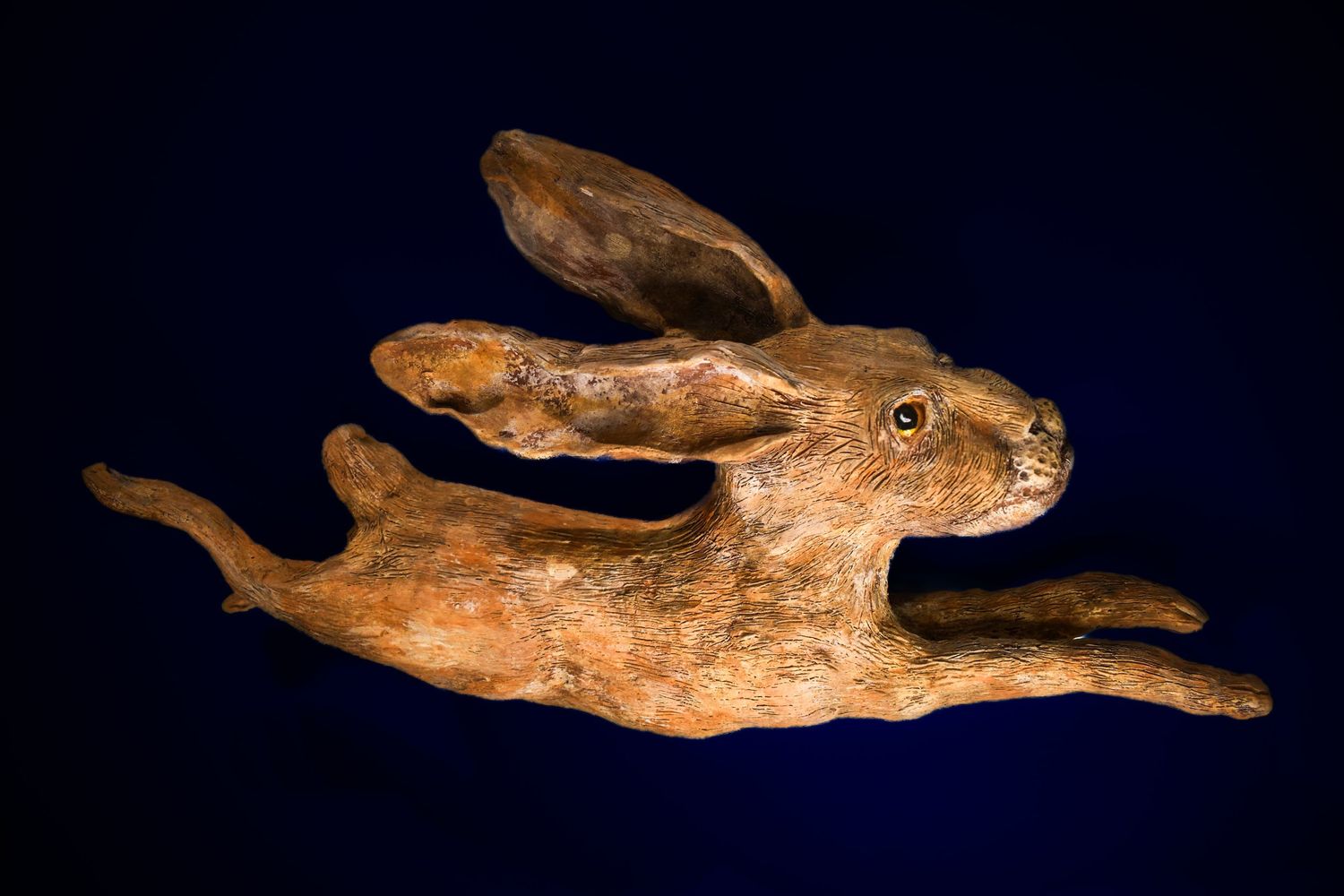 clay sculpture of a leaping hare against a dark blue background.