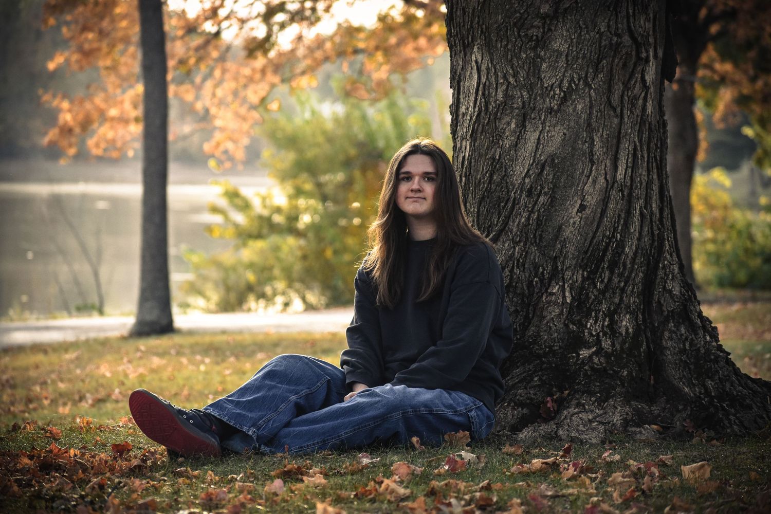 A dreamy autumn portrait taken against large tree trunk with golden leaves scattered on the ground.