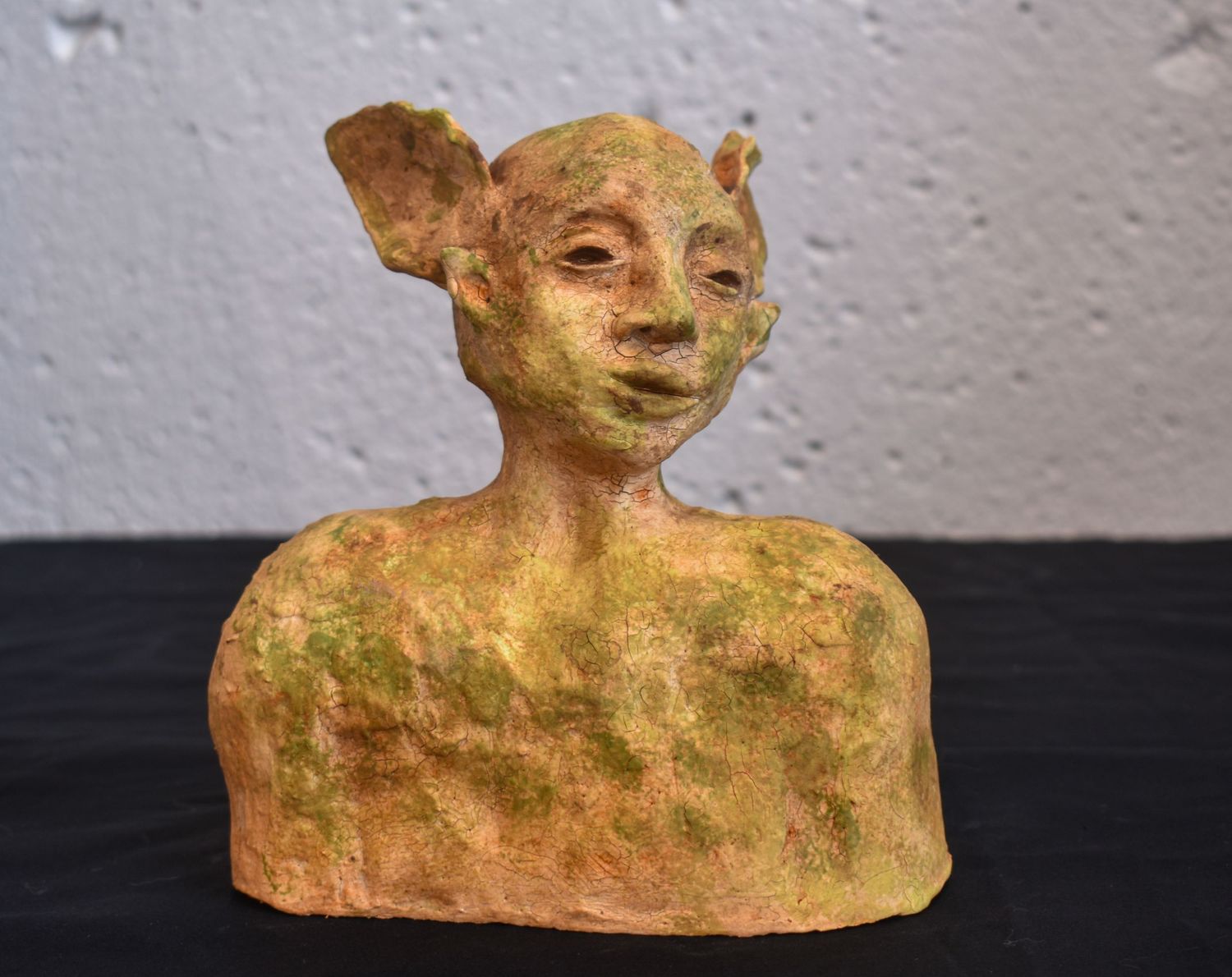 Weathered clay sculpture bust with textured surface and earthy tones,