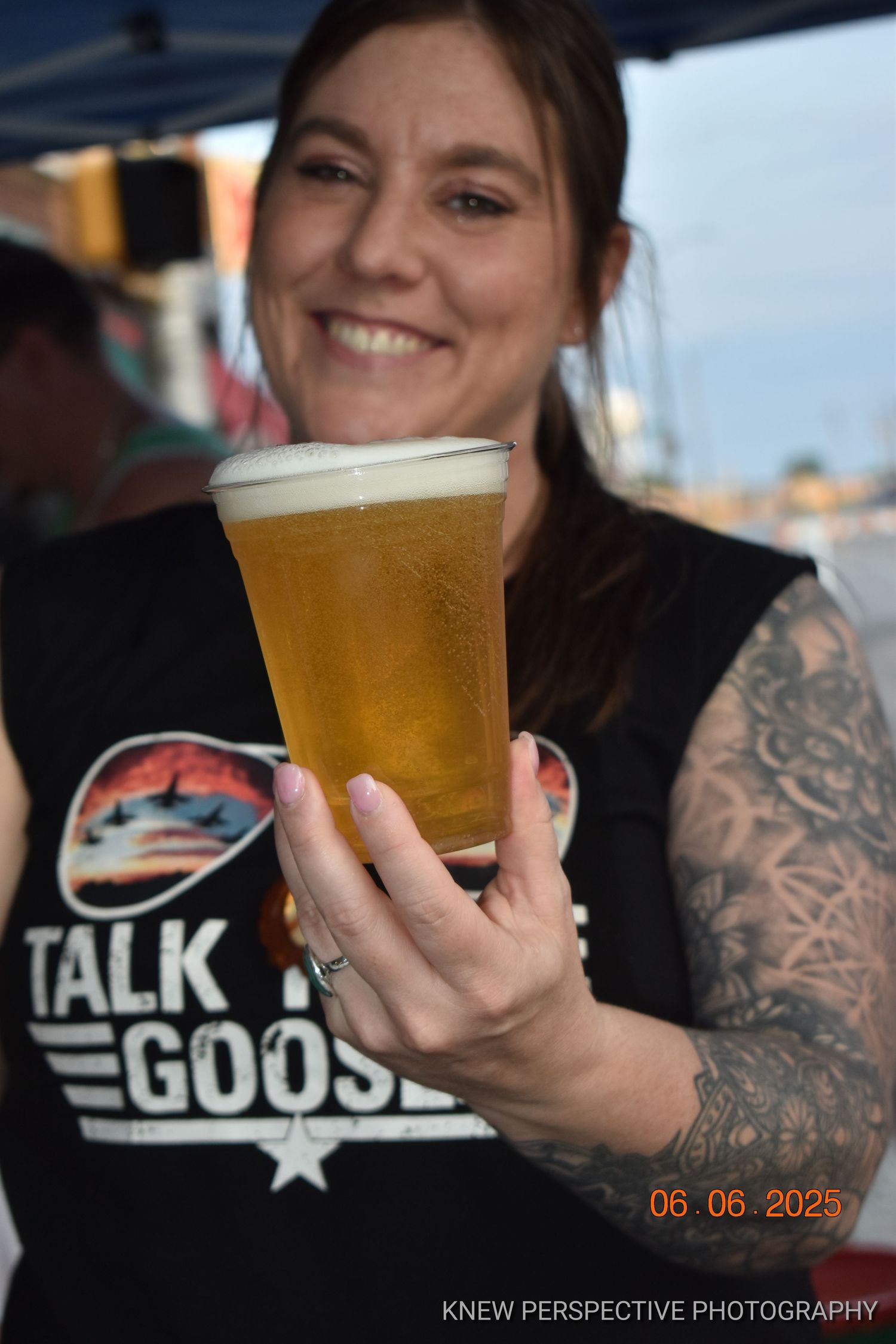 close-up shot showing a glass of golden beer being held by tattooed arms in black t-shirt.